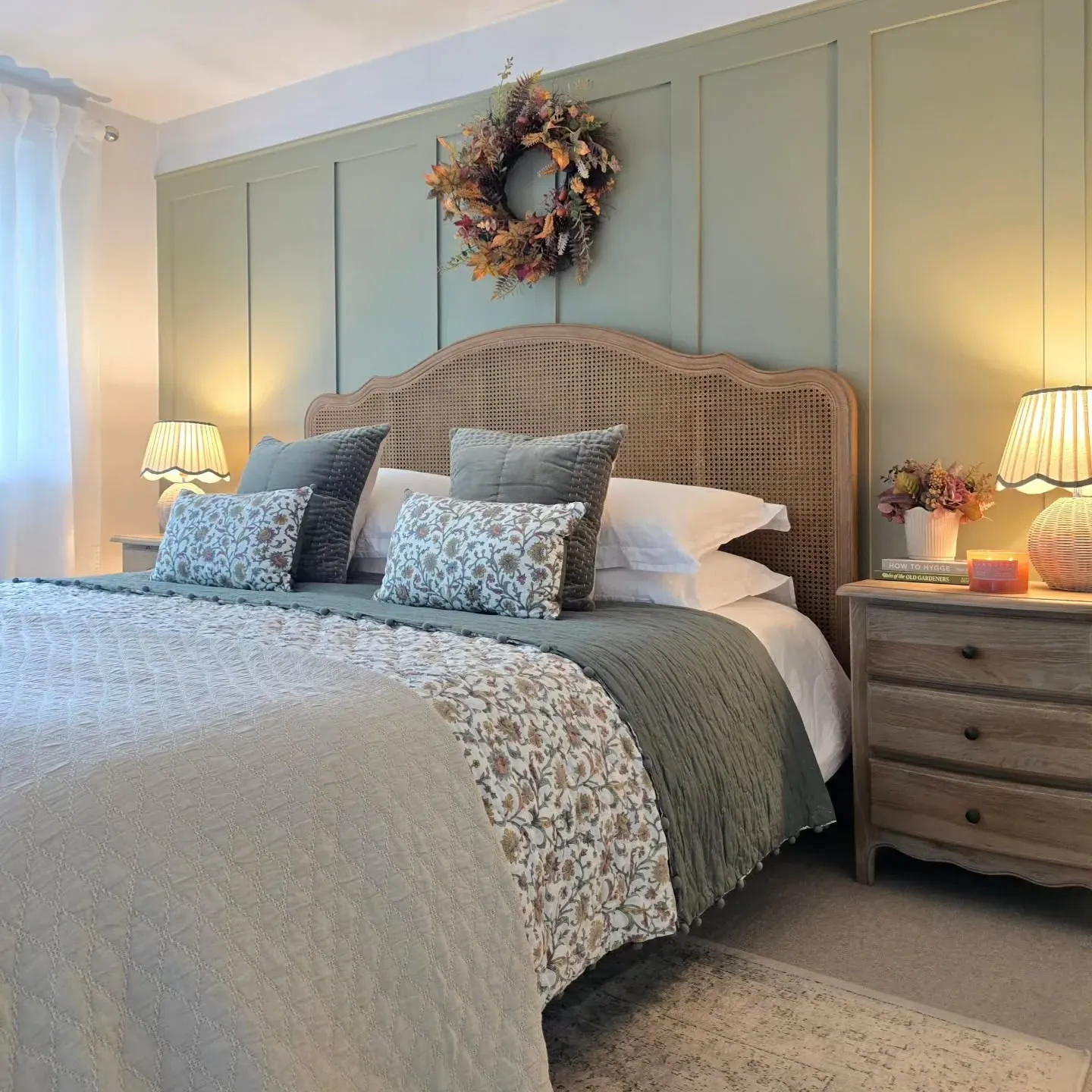 fall bedroom ideas with wreath above bed, sage paneling, floral bedding, blue pillows, and warm bedside lamps