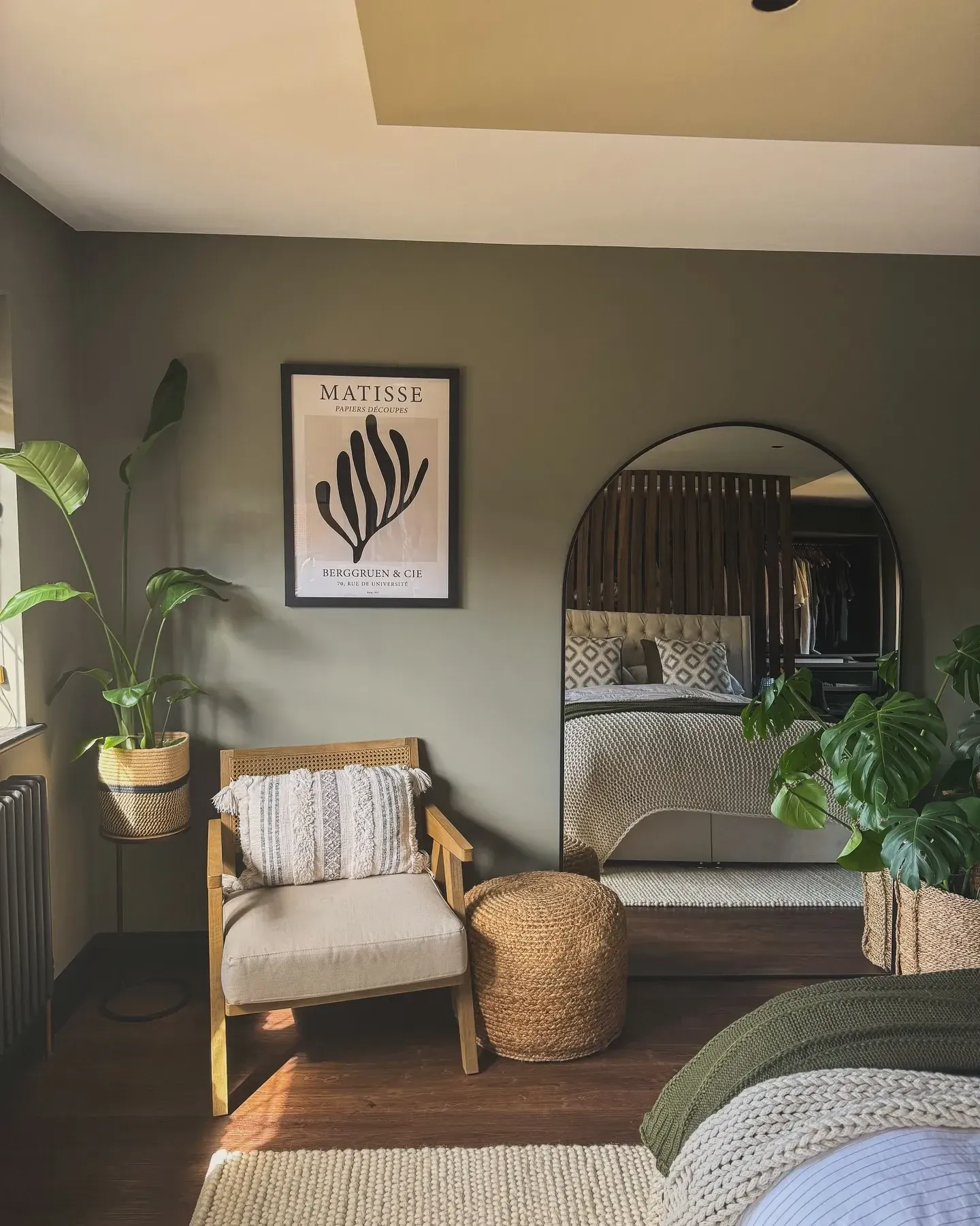 dark boho bedroom ideas with arched mirror, plants, woven basket, chair, and green bedding