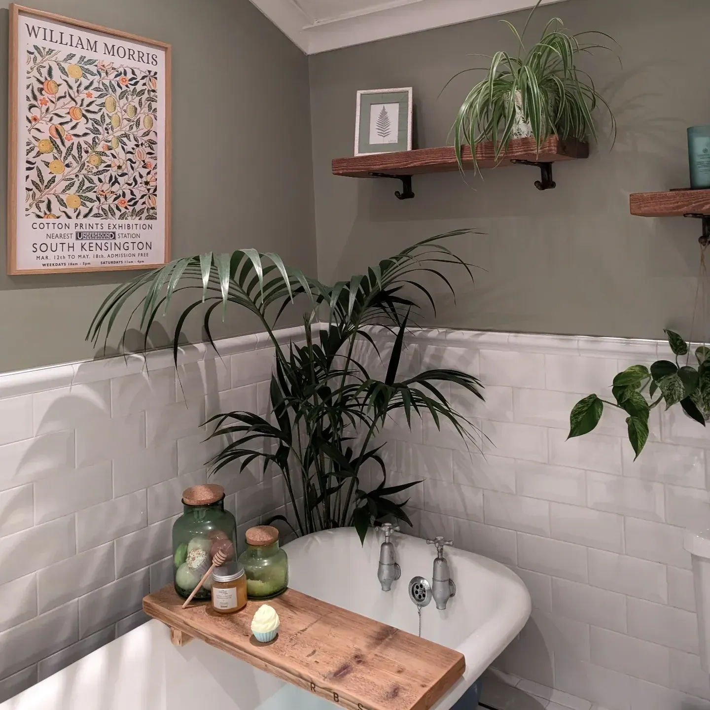 green bathroom ideas with dusty green half wall, bathtub, plants, floating shelves, candles, and wall art