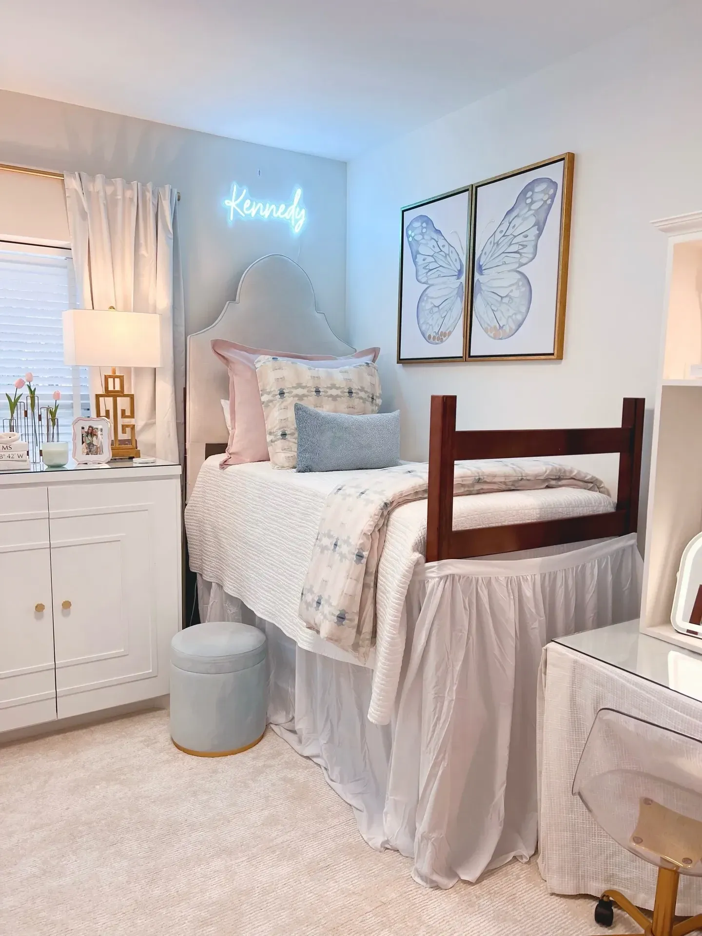 pink and blue dorm room ideas with blue butterfly wall art, pink bedding, blue ottoman, neon sign, and dorm desk