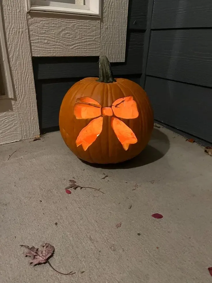 kid friendly pumpkin carving ideas with bow cutout, simple pumpkin face, and cute Halloween design