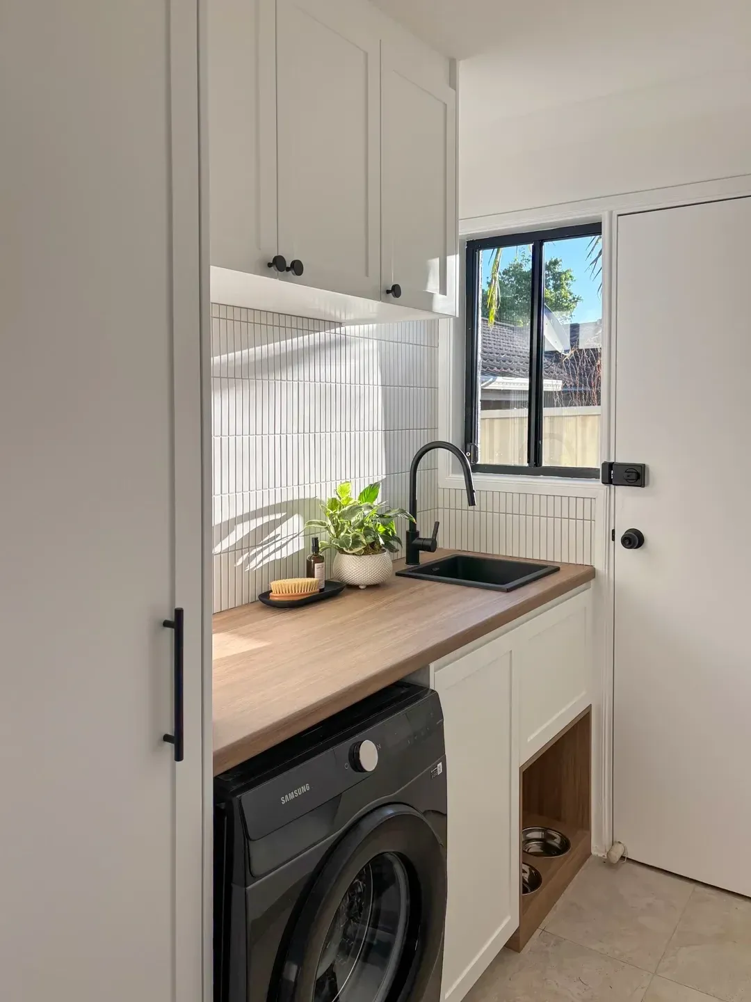 small laundry room ideas with wood counter, washer, sink, tall cabinet, and dog bowls built into the cupboard