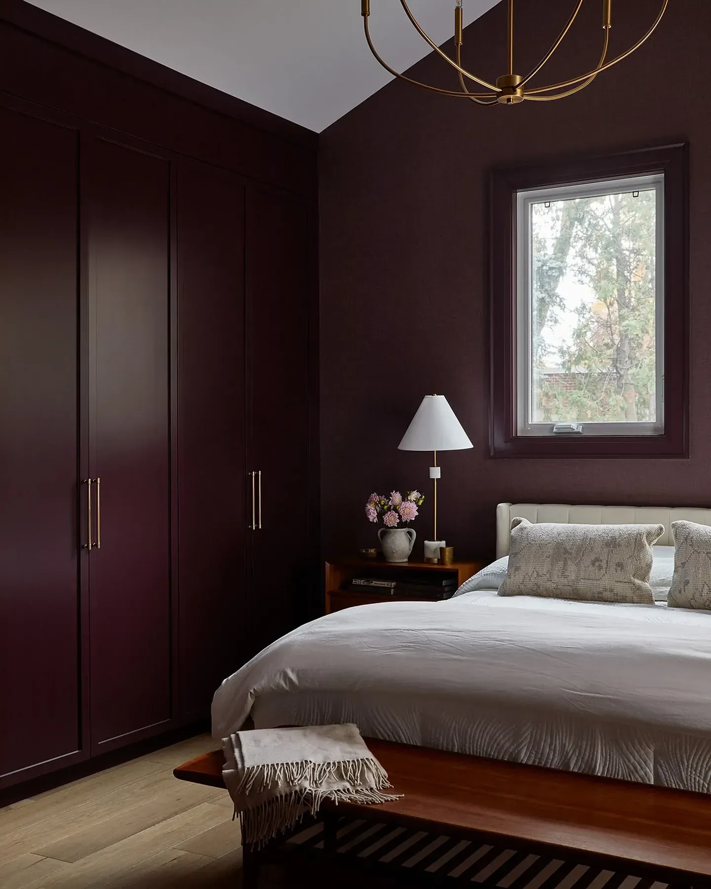 moody bedroom ideas with deep burgundy wardrobes, brass hardware, wood bed, white bedding, and black rug