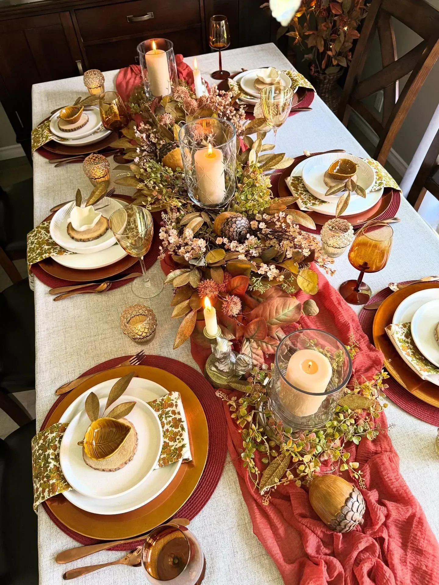 fall table decor ideas with burgundy napkins, candles, greenery, pumpkins, white plates, and layered fall place settings