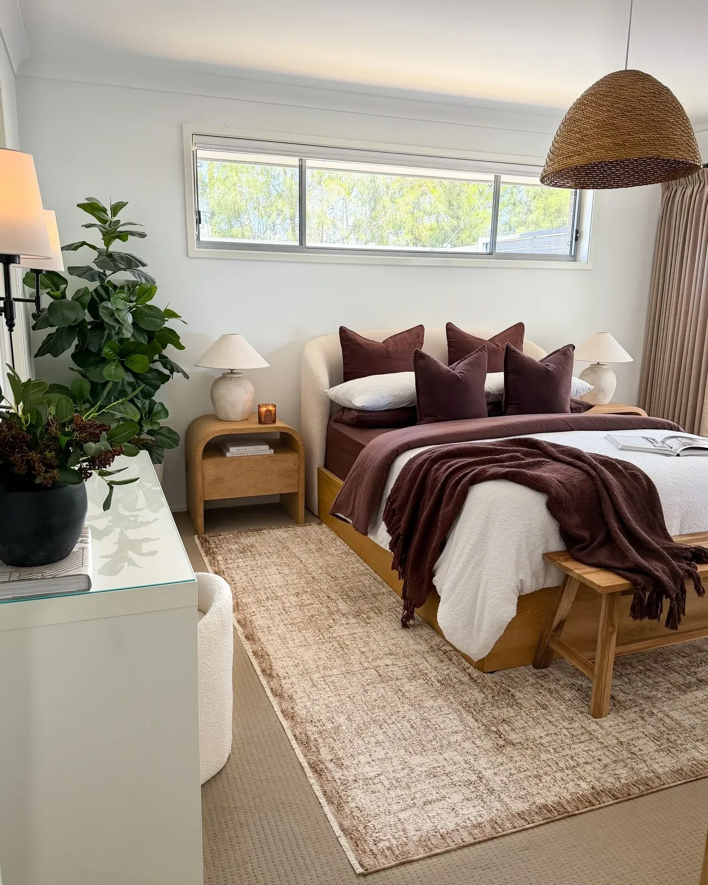 fall bedroom ideas with burgundy throw blanket, white bedding, woven pendant, wood nightstands, layered rug, and plants