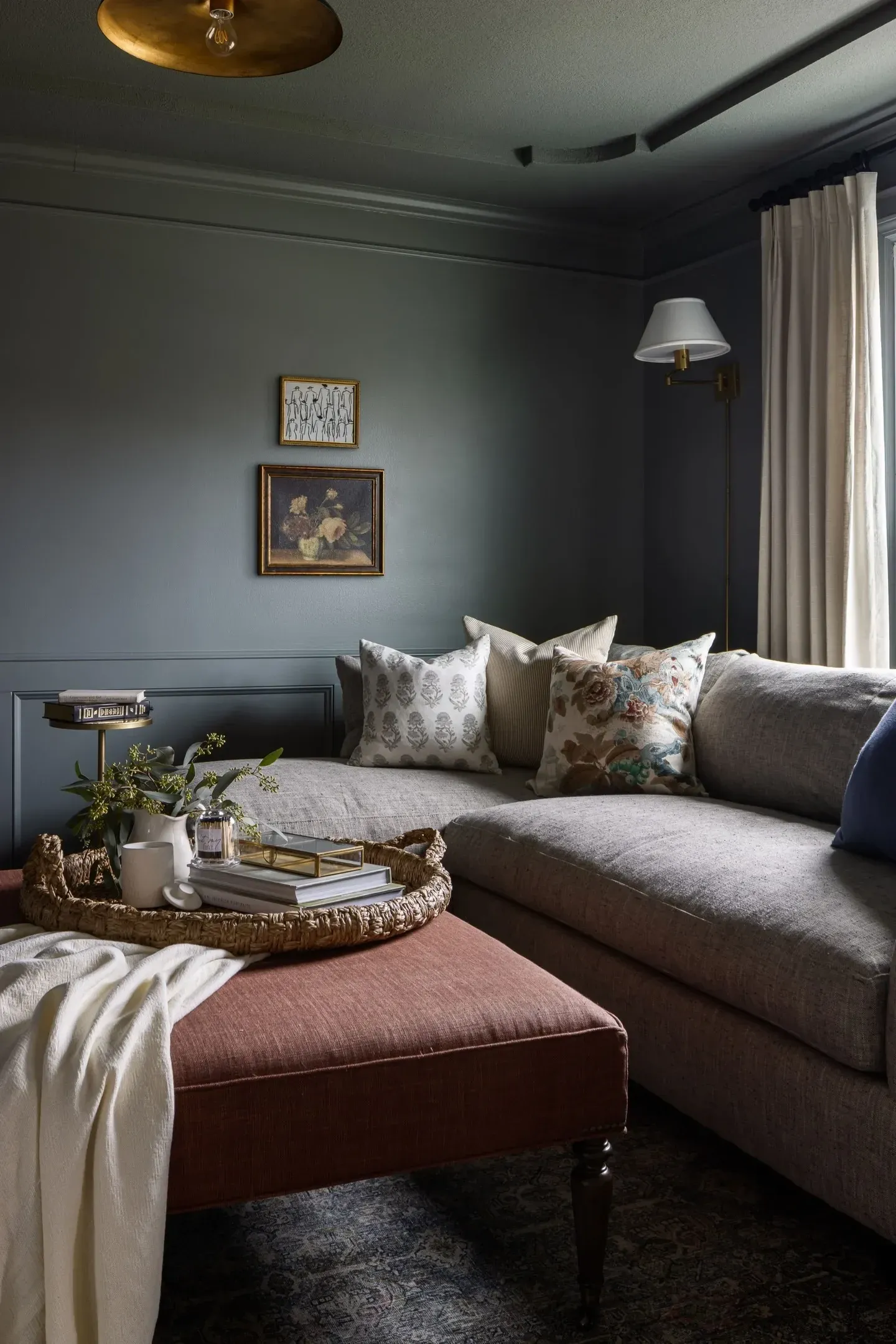 moody living room ideas with charcoal sectional, pink ottoman, layered pillows, and dark gray walls