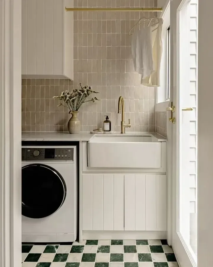 small laundry room ideas with checkerboard floor tile, brass hanging rail, farmhouse sink, washer, and small laundry storage