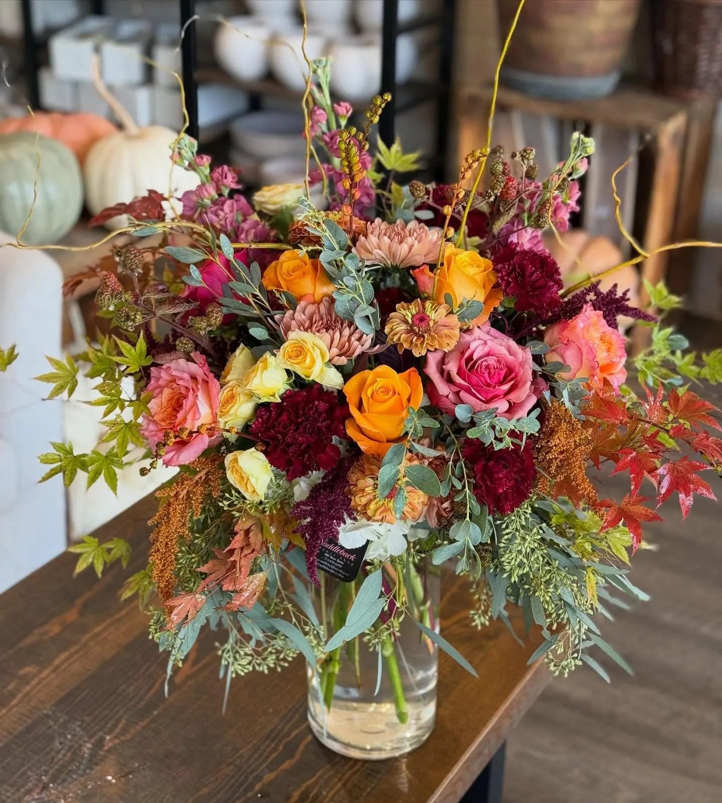 fall flower arrangement ideas with roses orange flowers burgundy stems and greenery in a glass vase
