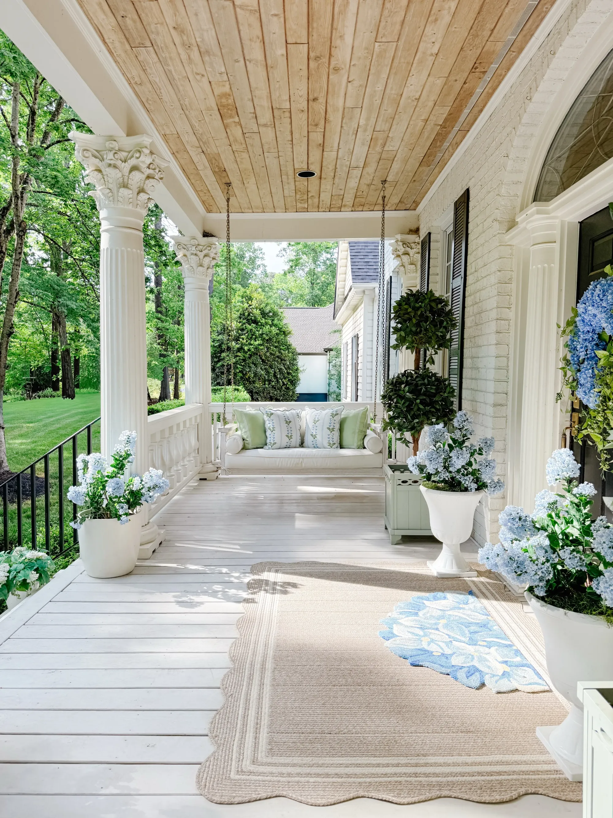 summer back porch decor ideas with covered porch, wood ceiling, white columns, blue accents, planters, and outdoor rug