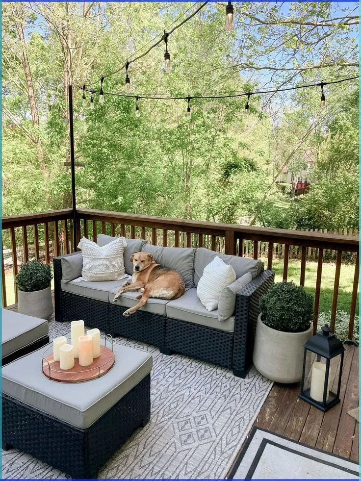 summer back porch decor ideas with small deck, outdoor sofa, pillows, candles, planters, and string lights