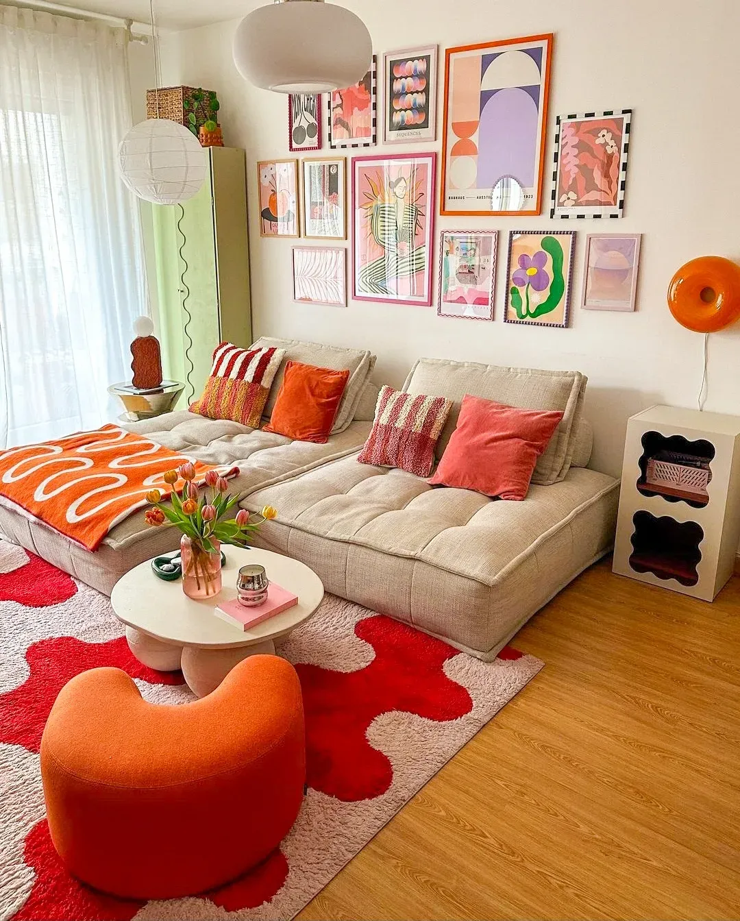 colorful living room ideas with colorful gallery wall, cream sofa, orange chair, red patterned rug, and playful art