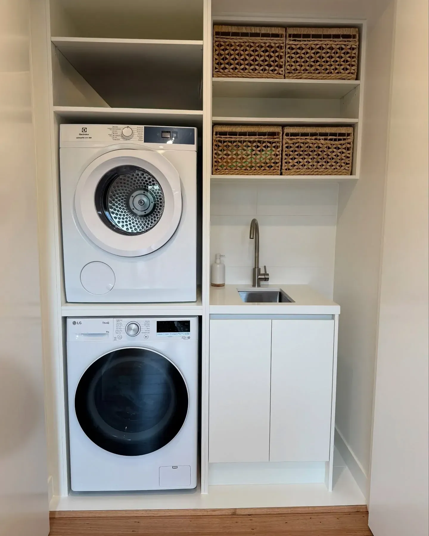 small laundry room ideas with stacked washer dryer, basket cubbies, small sink, white cabinets, and vertical laundry storage
