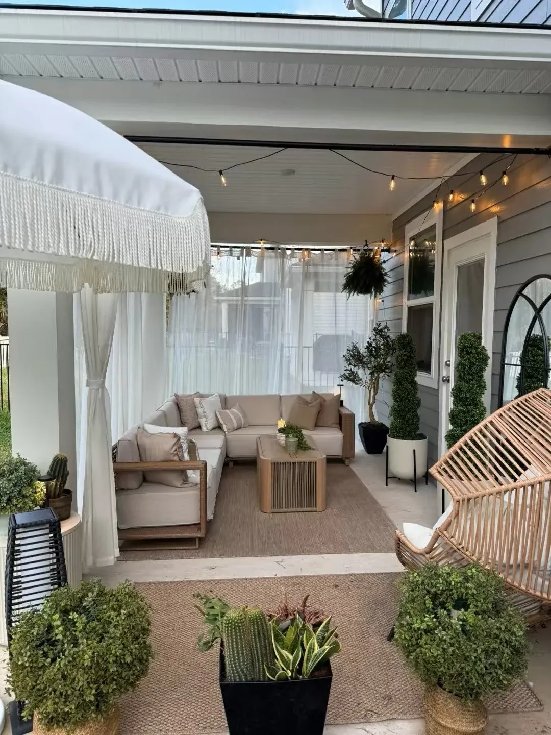 summer back porch decor ideas with white outdoor curtains, neutral seating, hanging chair, and potted plants