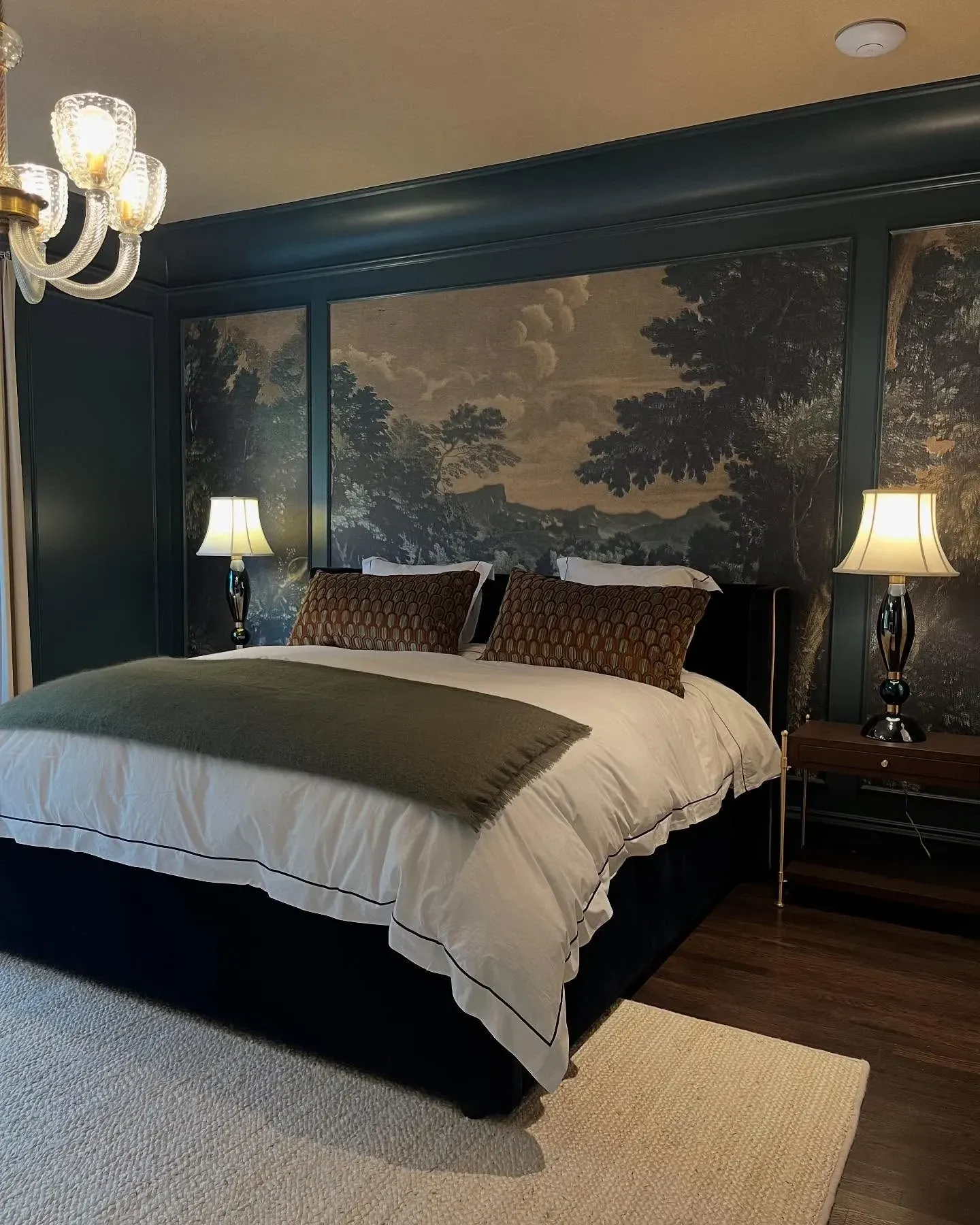 moody bedroom ideas with landscape mural, dark green trim, black bed, bedside lamps, and chandelier