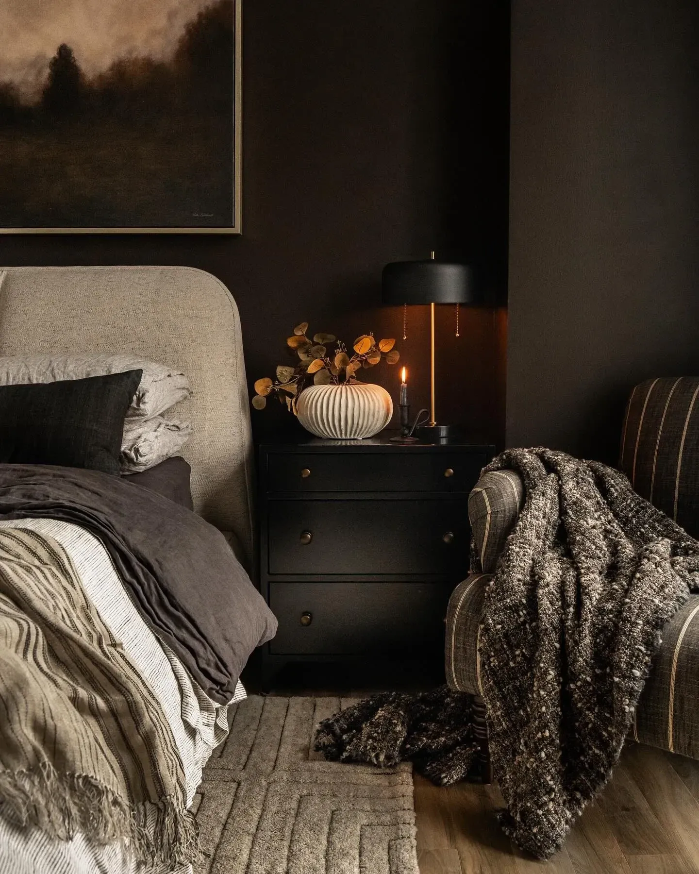 dark boho bedroom ideas with dark nightstand, warm lamp, pumpkin, textured throw, and layered bedding