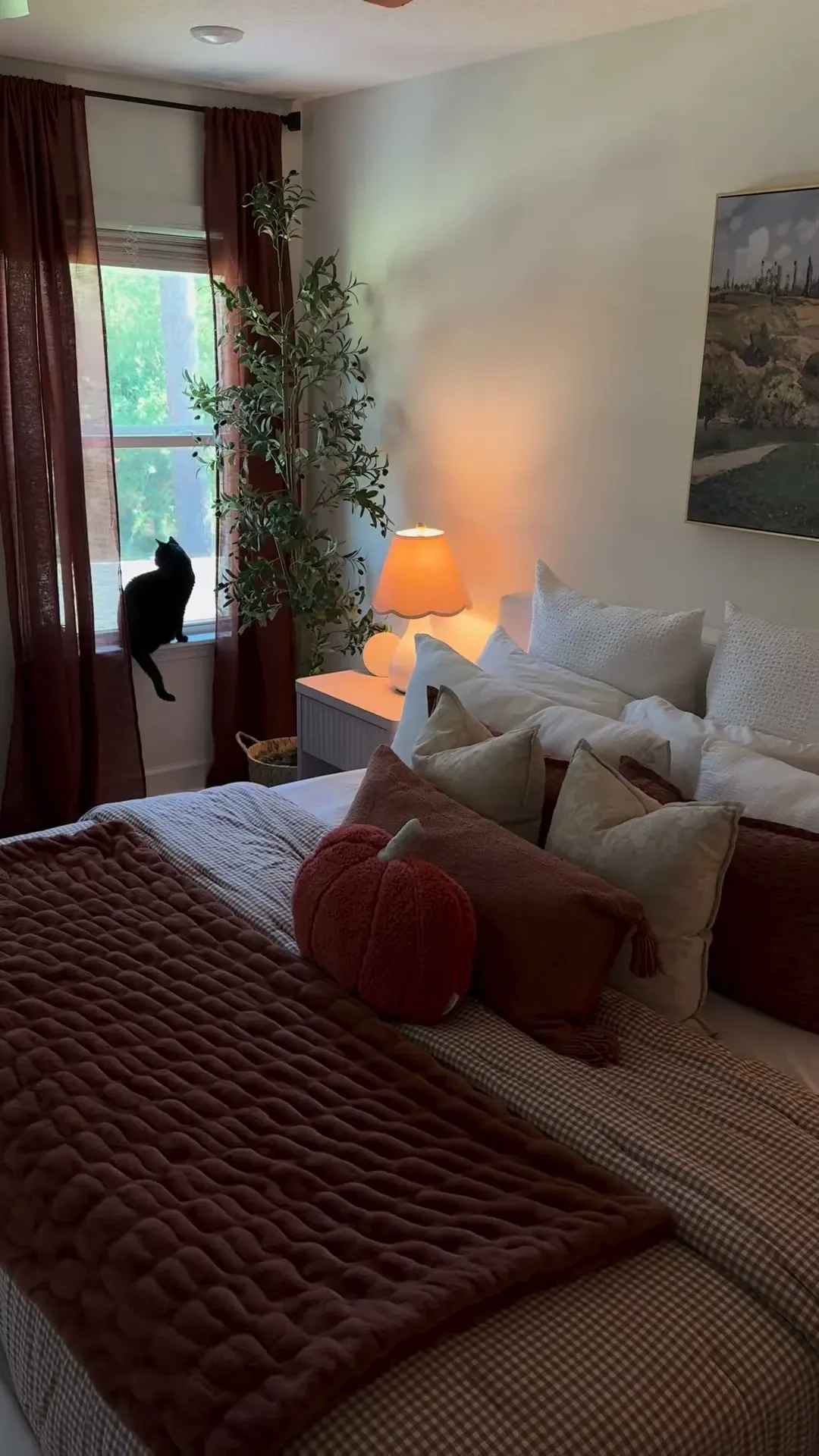 fall bedroom ideas with darker pumpkin pillow, rust throw blanket, deep curtains, warm bedside lamp, and cozy autumn bedding