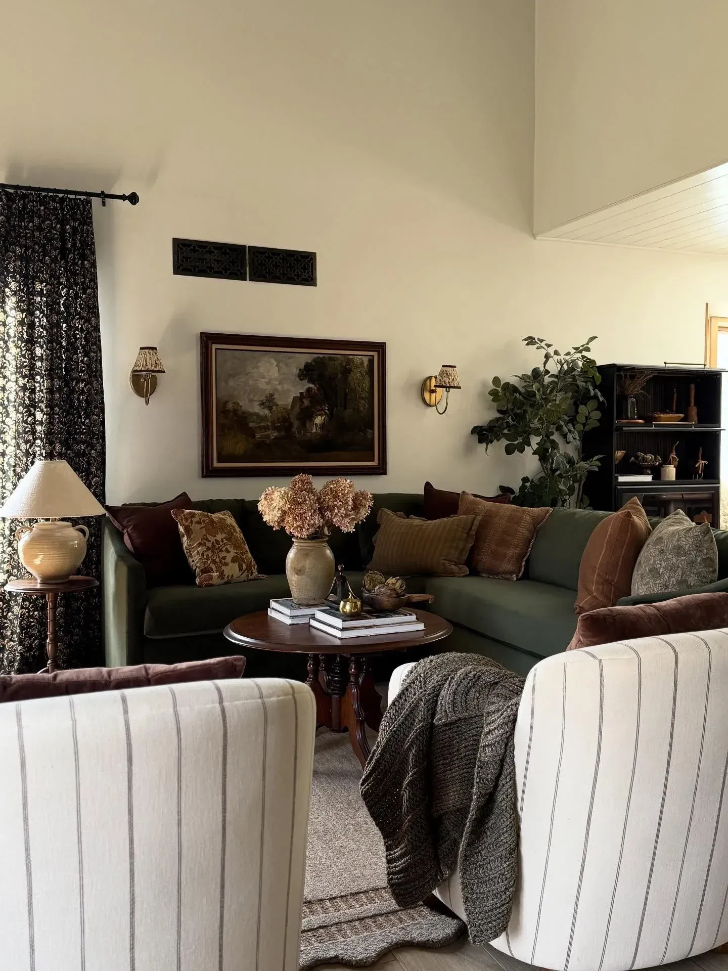 moody living room ideas with green sofa, patterned pillows, dark curtains, vintage art, and warm sconces