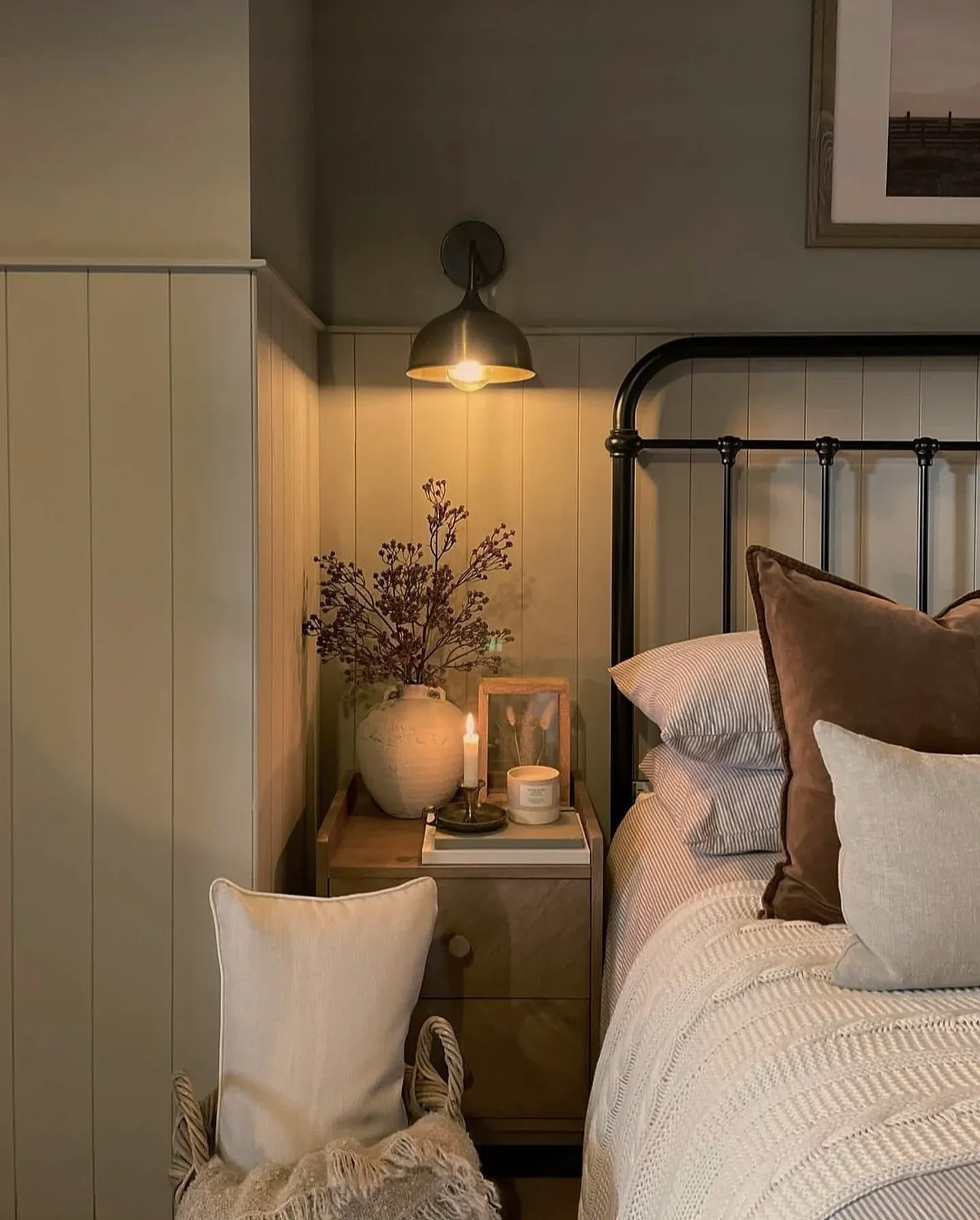 fall bedroom ideas with dark flowers, black metal bed, wall lamp, brown pillow, and warm bedside lighting