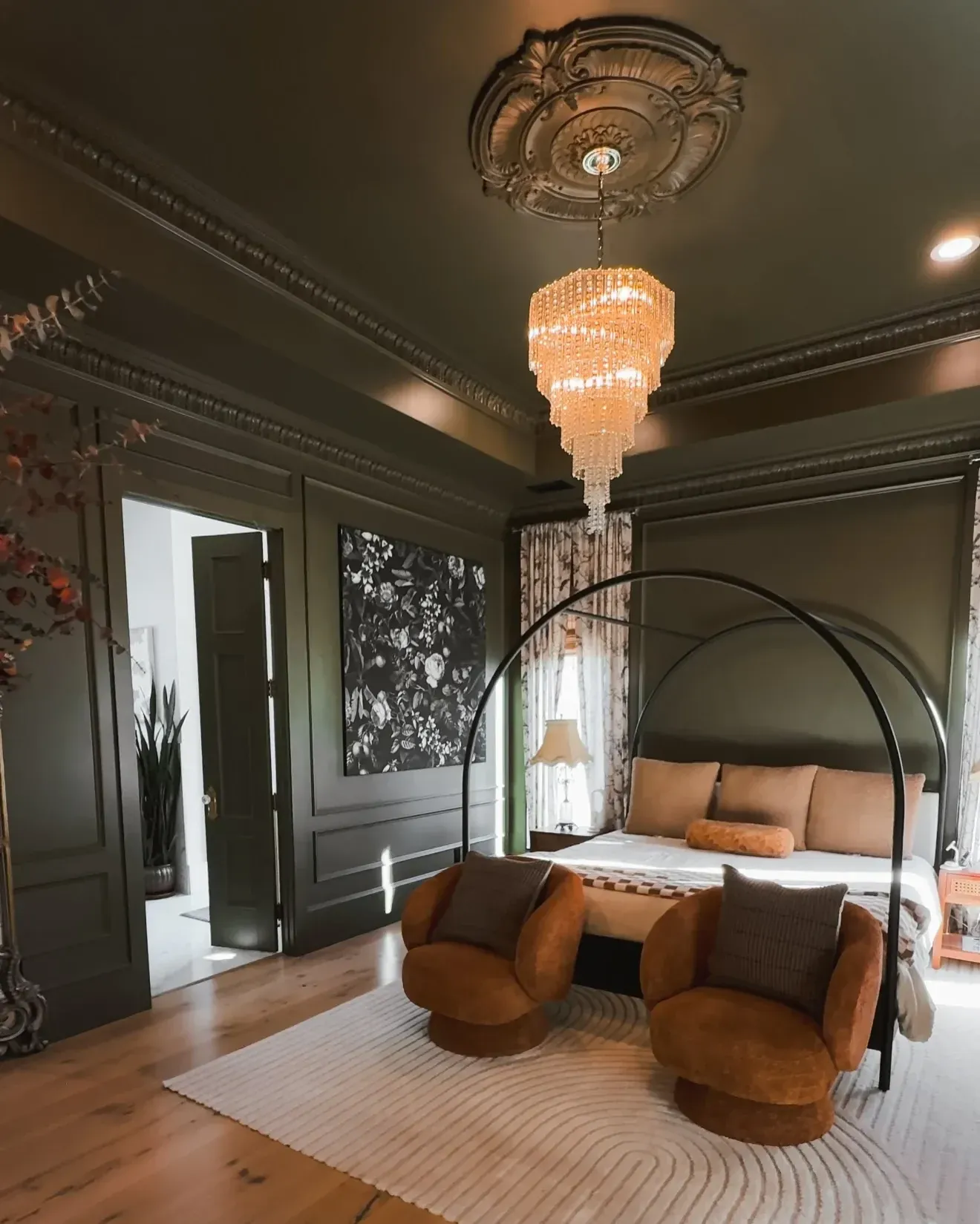 moody bedroom ideas with dark trim, chandelier, patterned wall panels, curved chairs, and warm wood floors