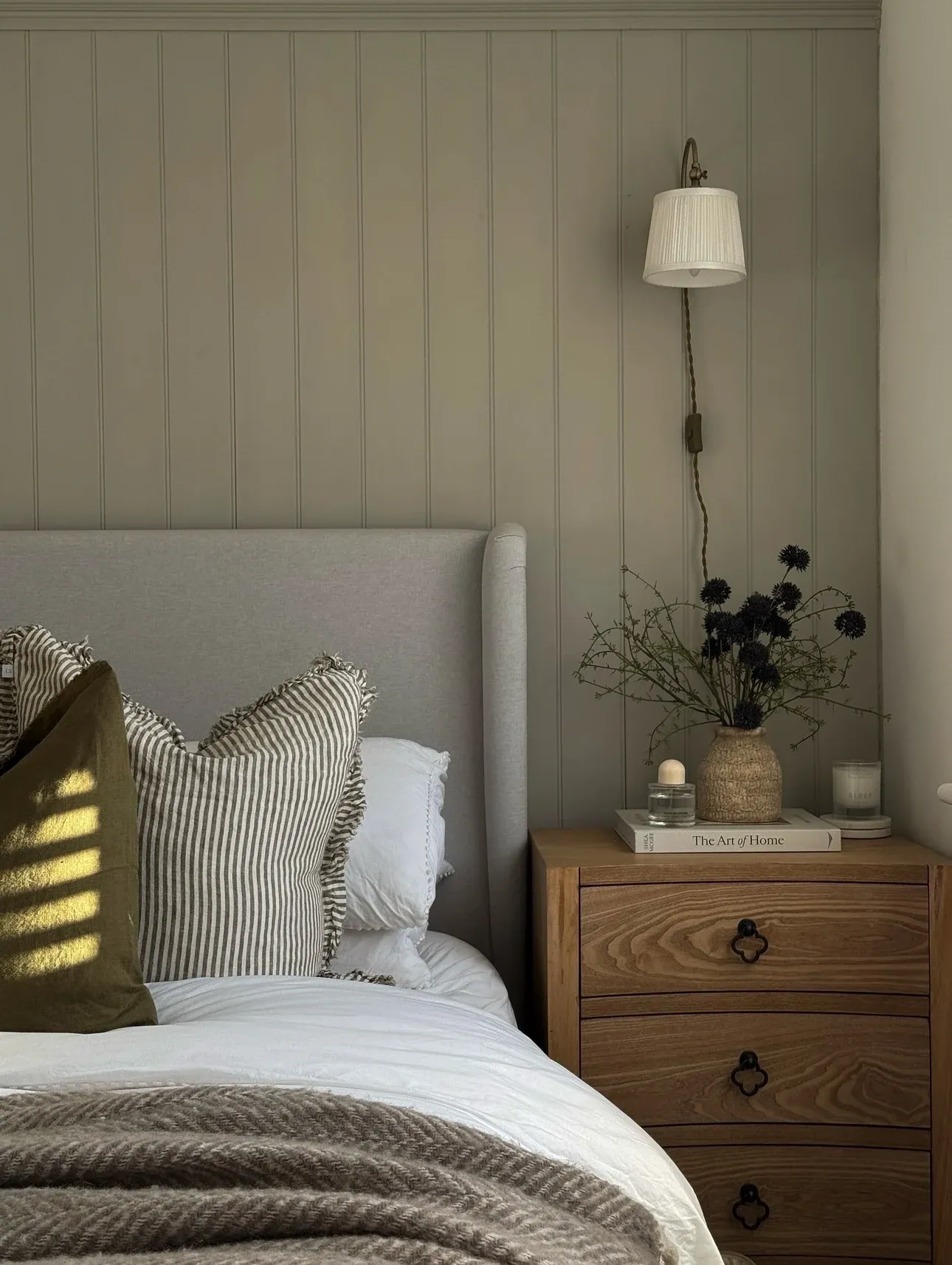 fall bedroom ideas with sage paneling, striped pillow, wood nightstand, neutral bedding, and earthy fall bedroom decor