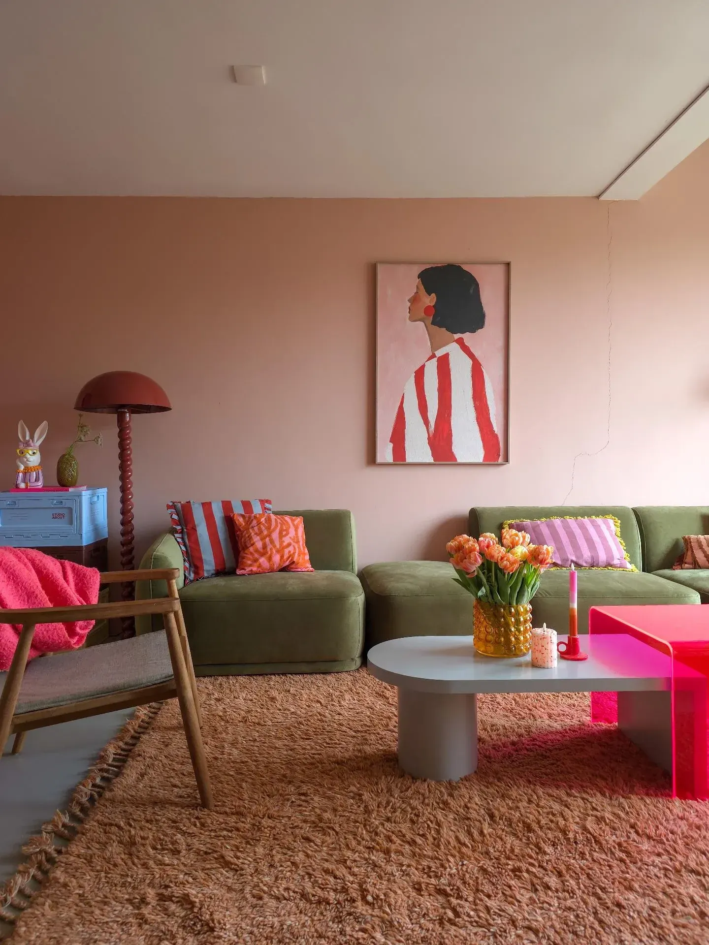 colorful living room ideas with earthy tones, olive green sofa, peach wall, terracotta rug, wood chair, and pink coffee table