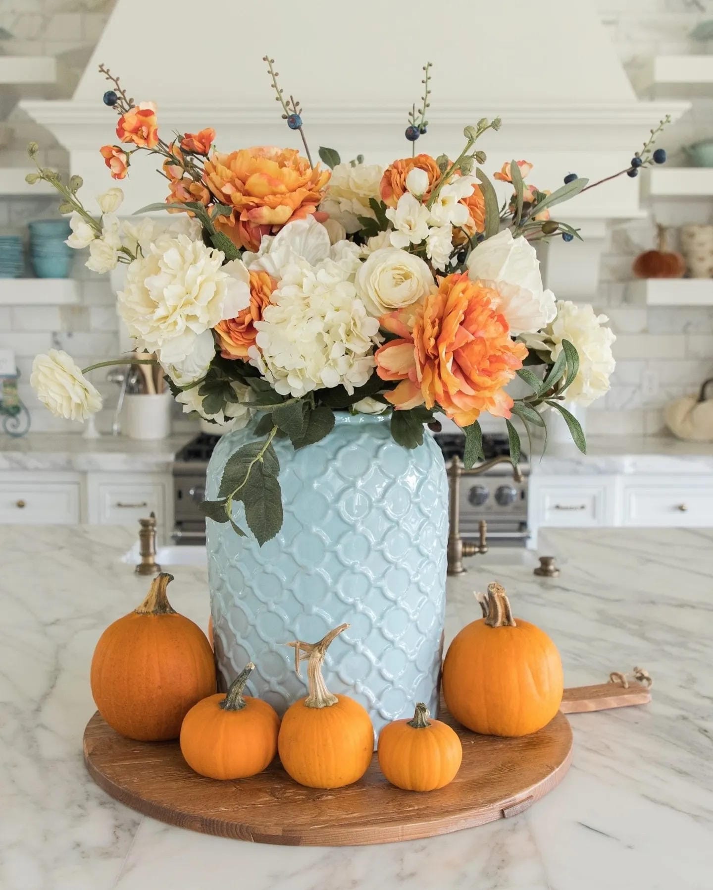 fall flower arrangement ideas with orange and white flowers in a blue vase surrounded by pumpkins