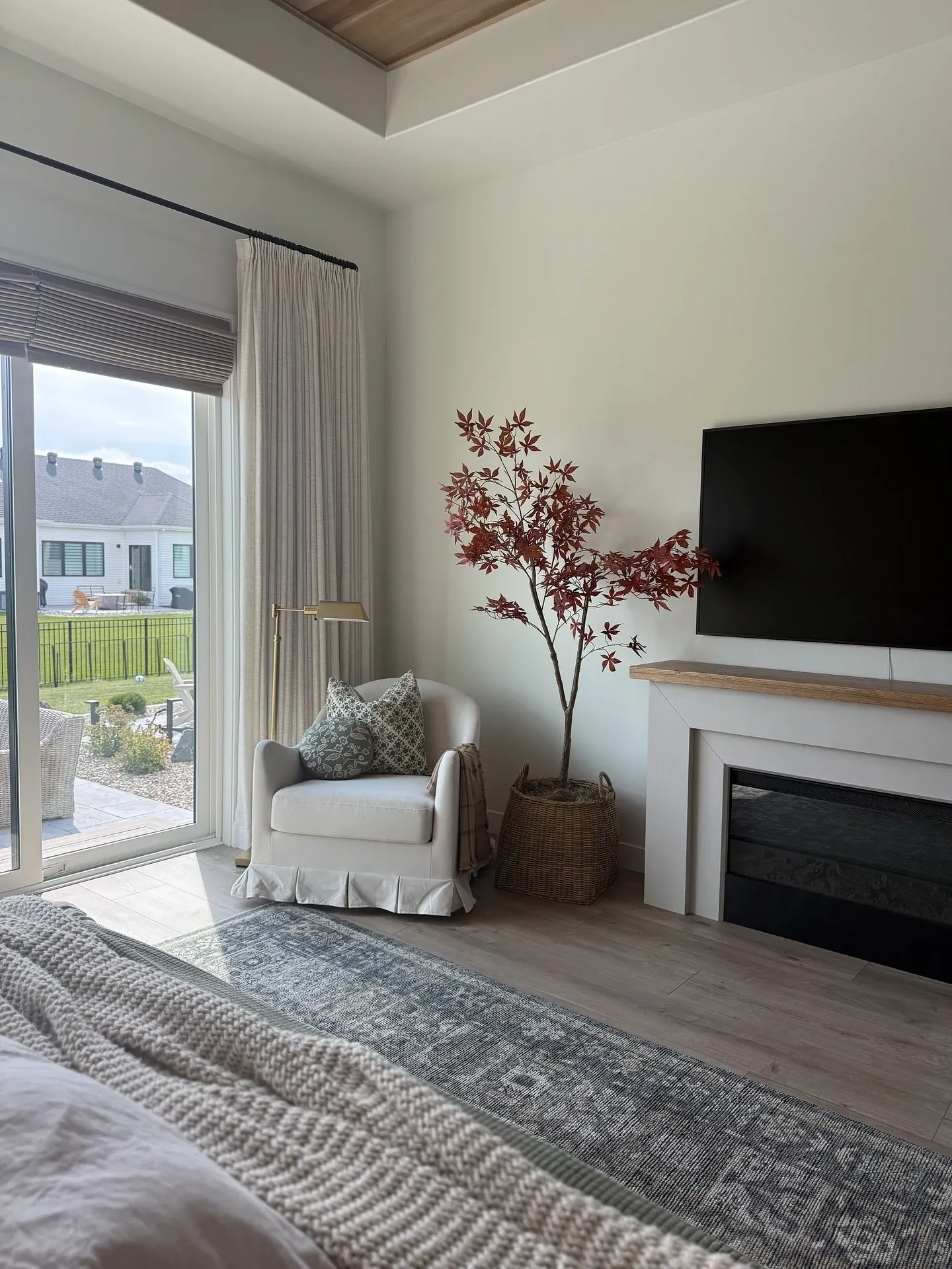 fall bedroom ideas with fall tree beside fireplace, woven basket planter, cozy chair, neutral bedroom, and soft rug