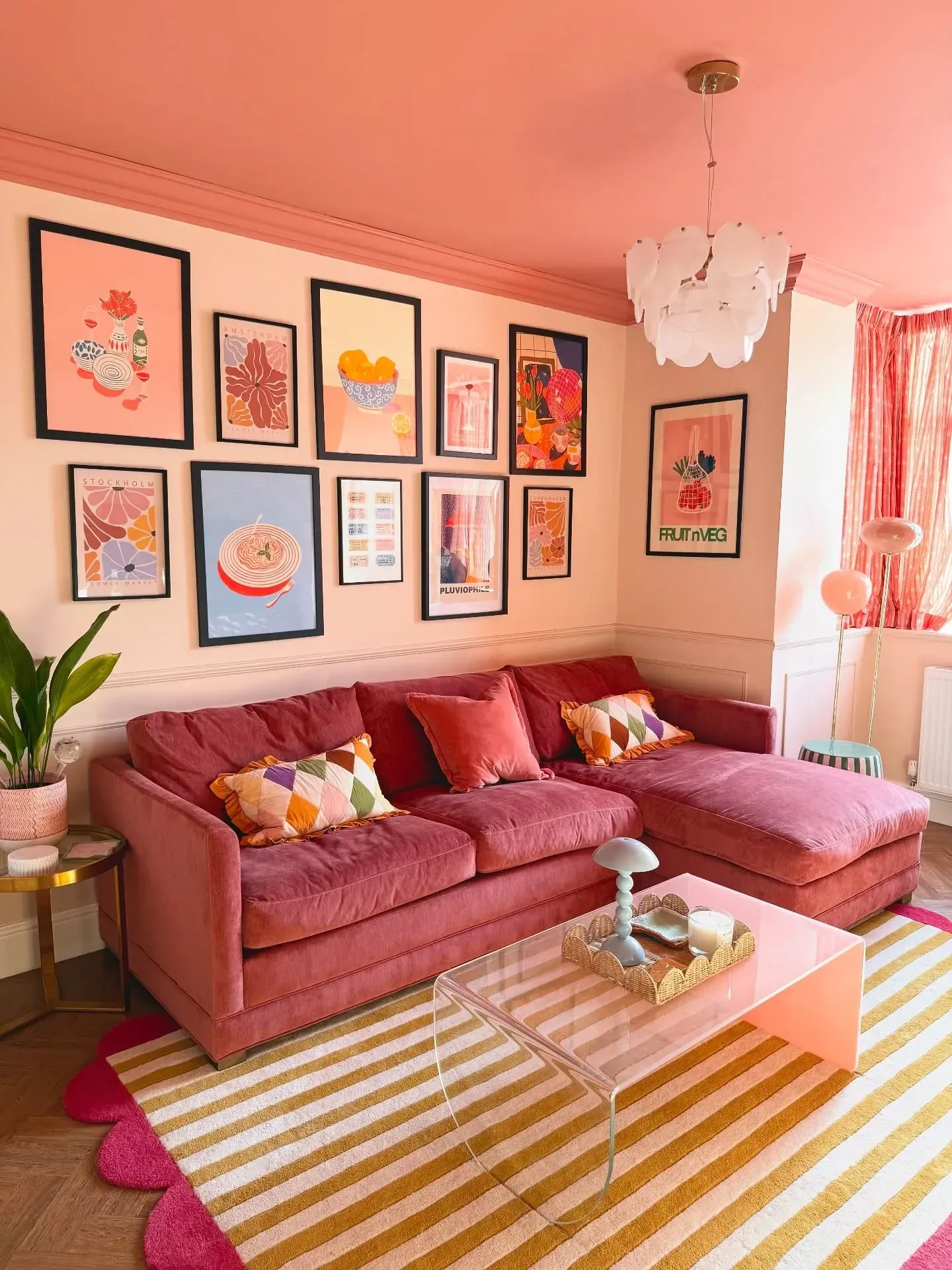 colorful living room ideas with pink sofa, pink walls, gallery wall, striped rug, and bright pillows
