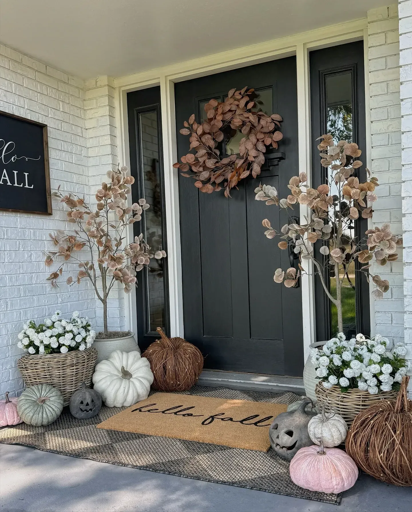 fall porch decor ideas with pale pumpkins, white flowers, fall wreath, woven baskets, black front door, and layered doormat