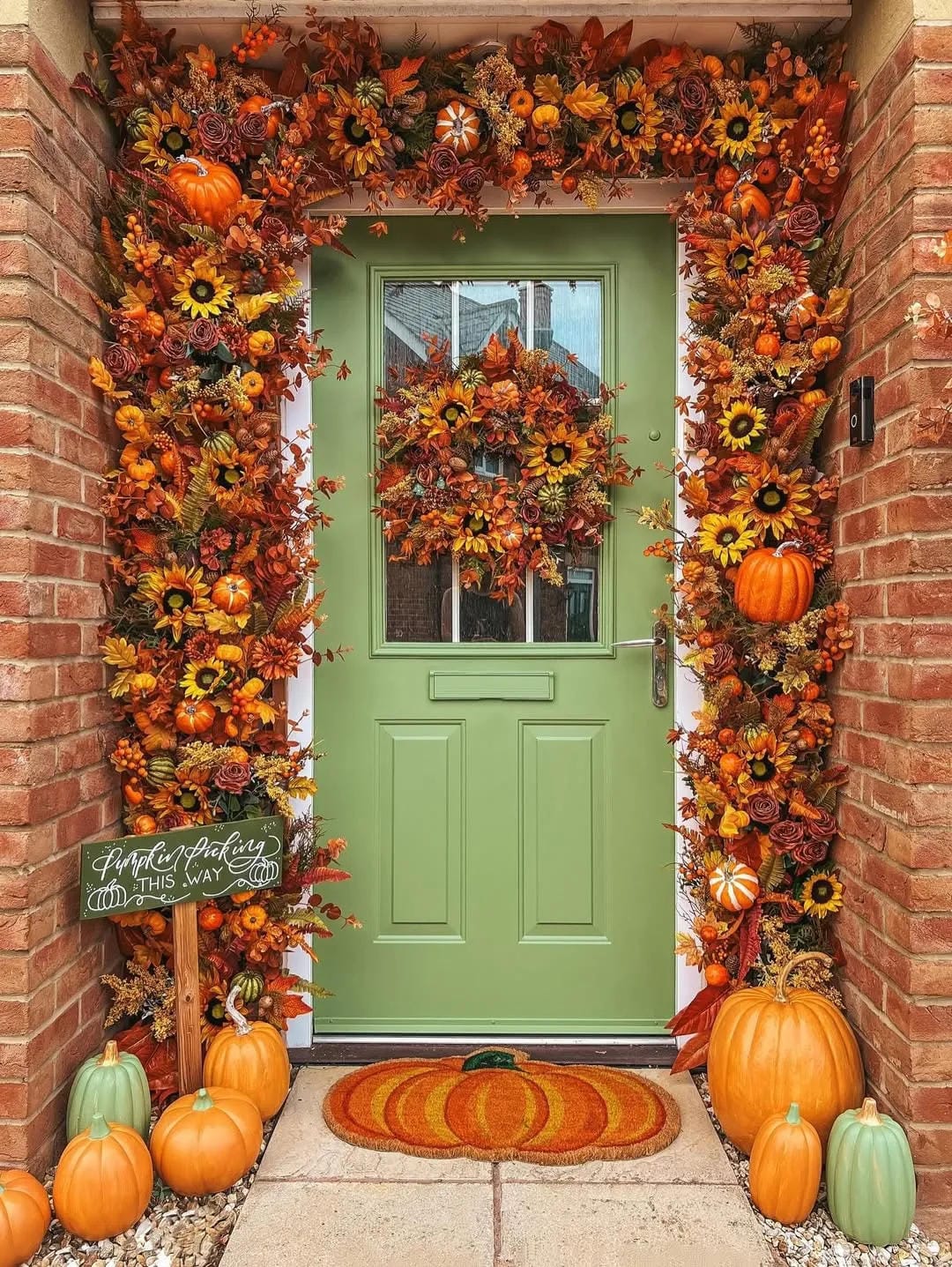 fall front door decor ideas with green door, full fall garland, pumpkins, wreath, and pumpkin doormat
