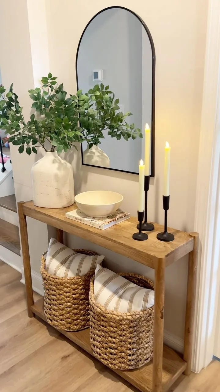 fall entryway table decor ideas with greenery in a white vase, arched mirror, black candlesticks, bowl, books, and baskets