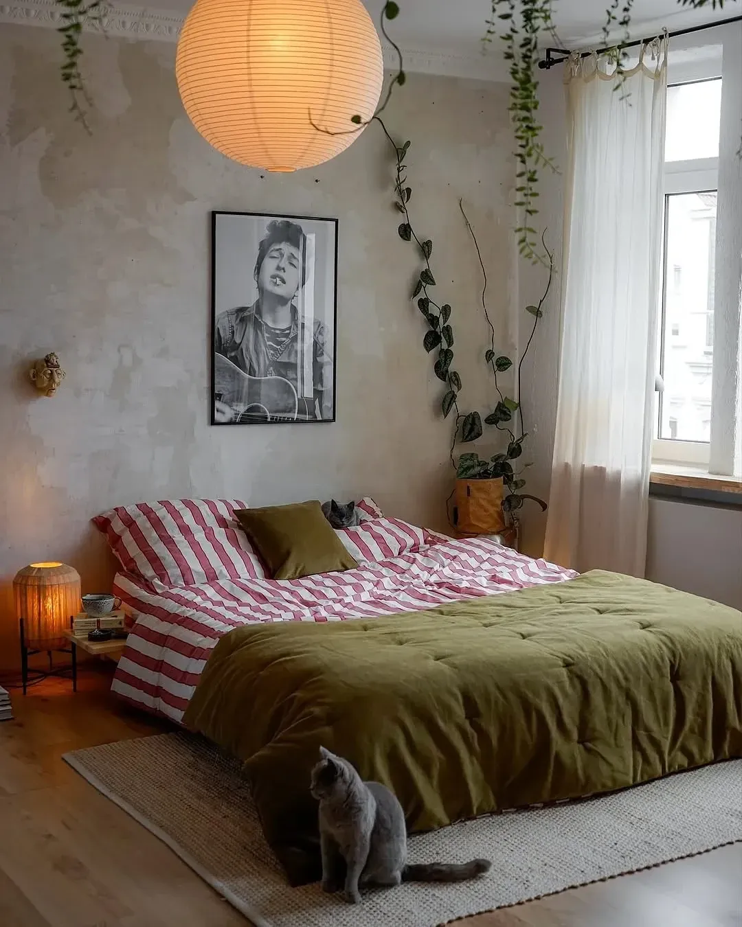 dark boho bedroom ideas with olive bedding, paper lantern, plants, striped bedding, and warm floor lamp