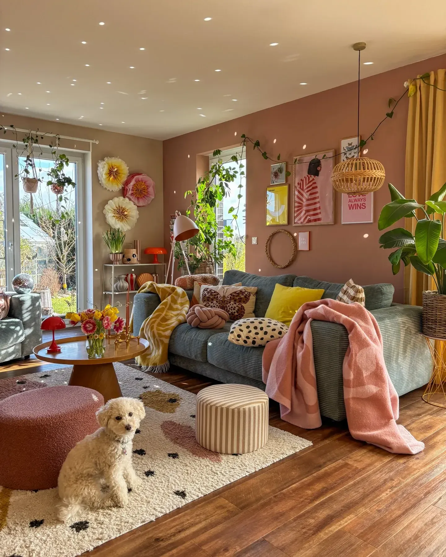 colorful living room ideas with pink walls, green sofa, yellow pillows, plants, poufs, and warm wood floors