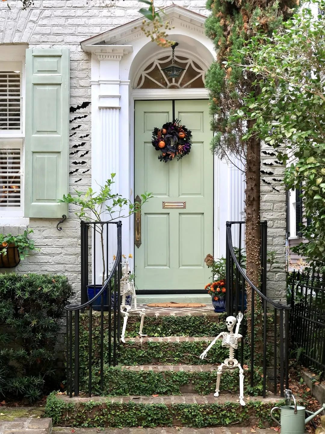 fall front door decor ideas with pale green door, wreath, pumpkins, plants, and skeleton decorations