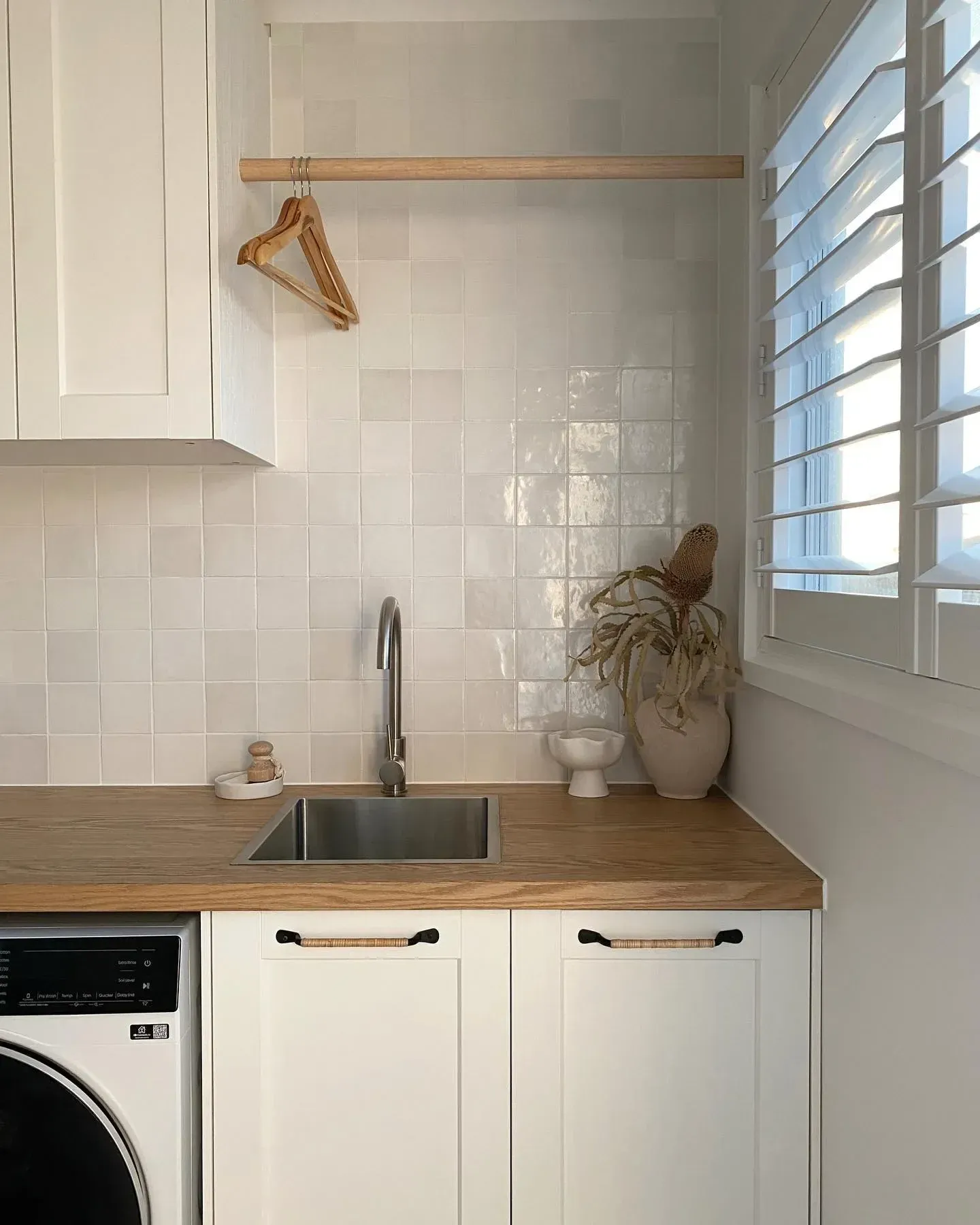 small laundry room ideas with coat hangers, wood counter, white cabinets, sink, and small laundry organization