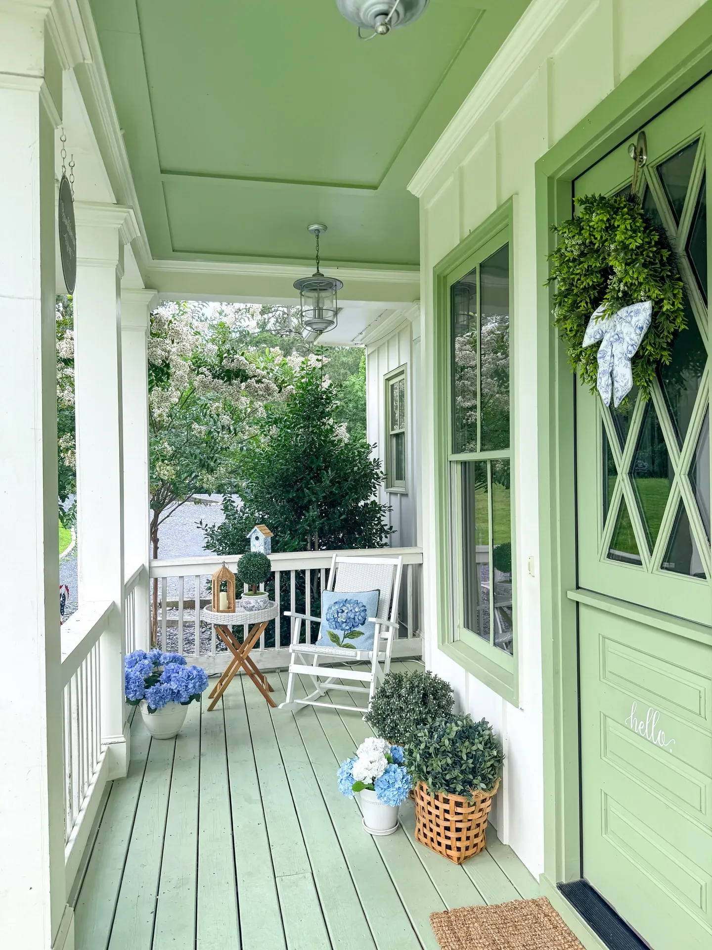 summer back porch decor ideas with blue hydrangeas, green wreath, blue ribbon, white chair, and basket planters