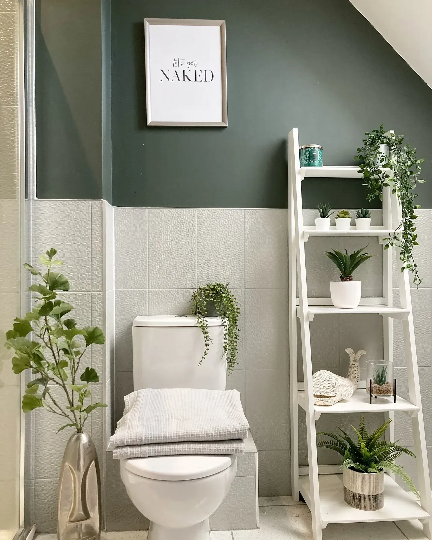 green bathroom ideas with dark green half wall, white tile, ladder shelf, plants, and framed print