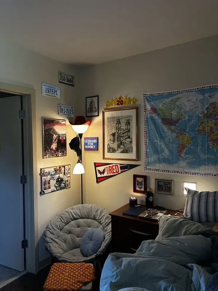 dorm decorating ideas for guys with large map wall decor, posters, gray chair, dark bedding, and desk area