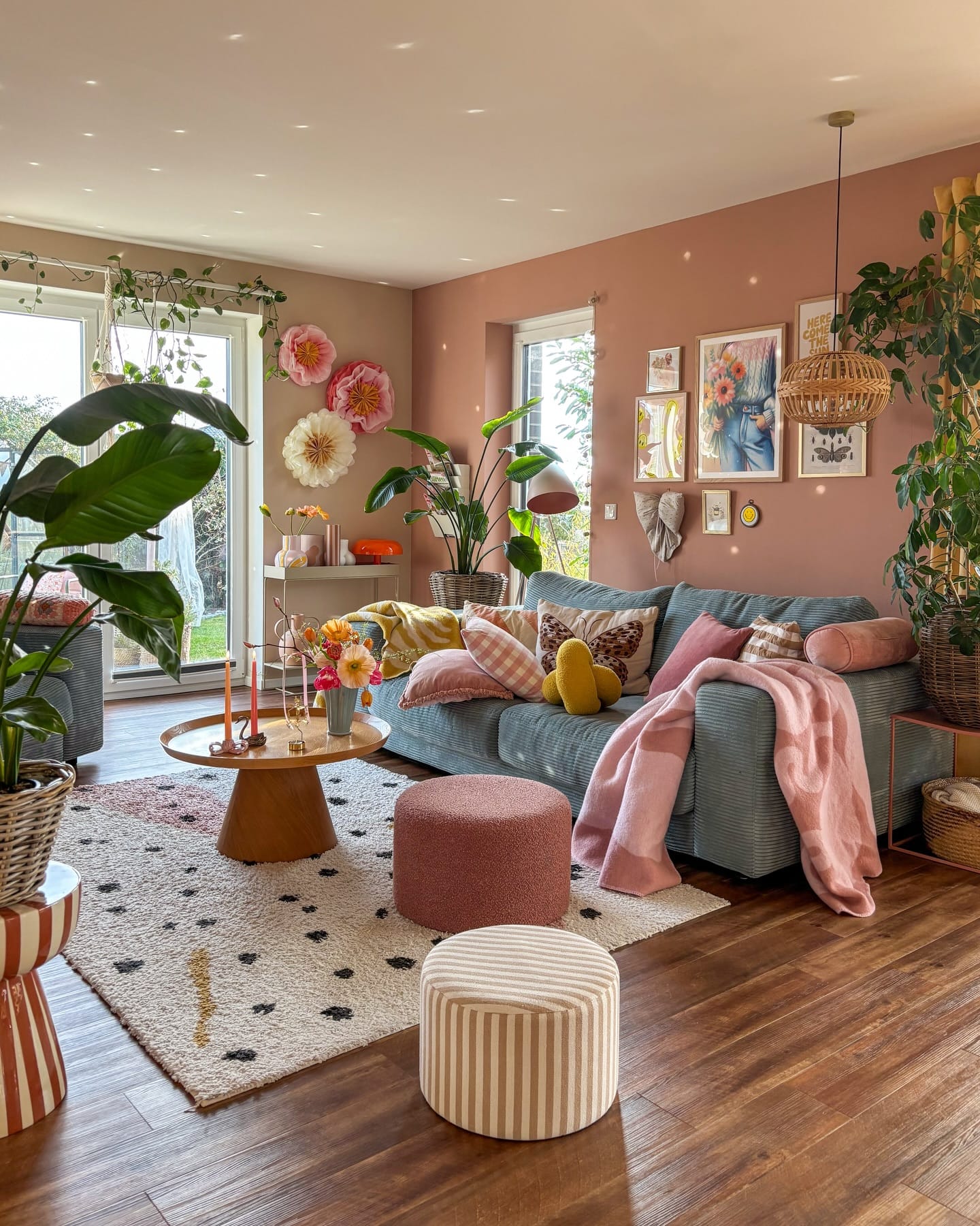 colorful living room ideas with green sofa, pink throw, plants, gallery wall, flowers, and patterned rug