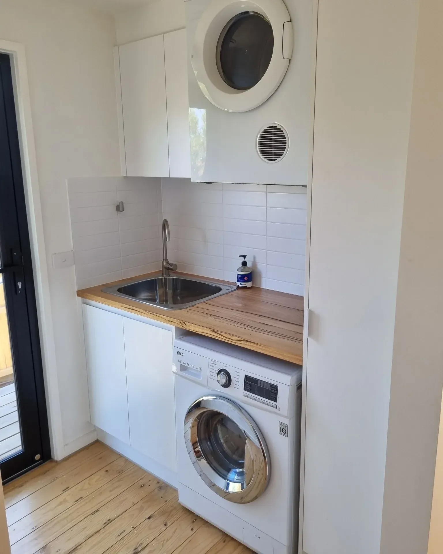 small laundry room ideas with compact washer dryer, tiny sink, wood counter, white cabinets, and small laundry layout