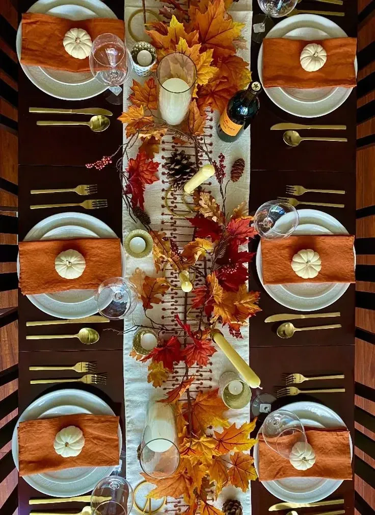 fall table decor ideas with mini pumpkins at each place setting, orange napkins, leaf garland, candles, and pinecones