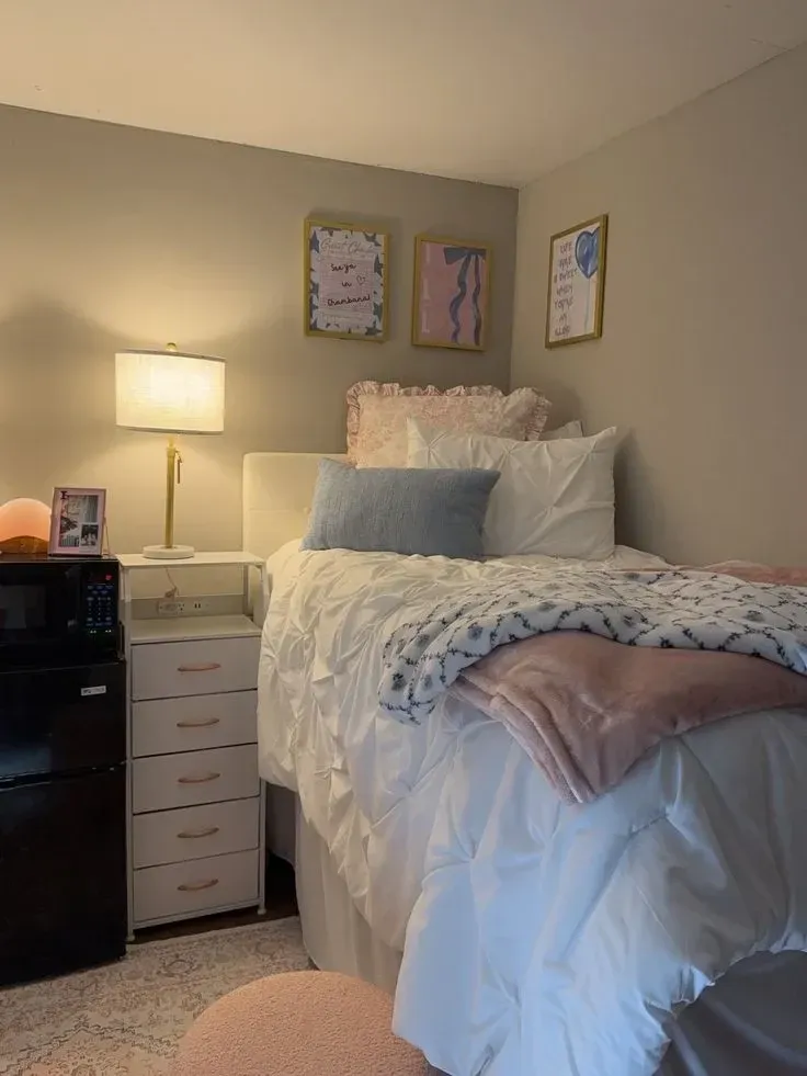 pink and blue dorm room ideas with blue pillow, pink throw blanket, white bedding, wall prints, and small dorm nightstand