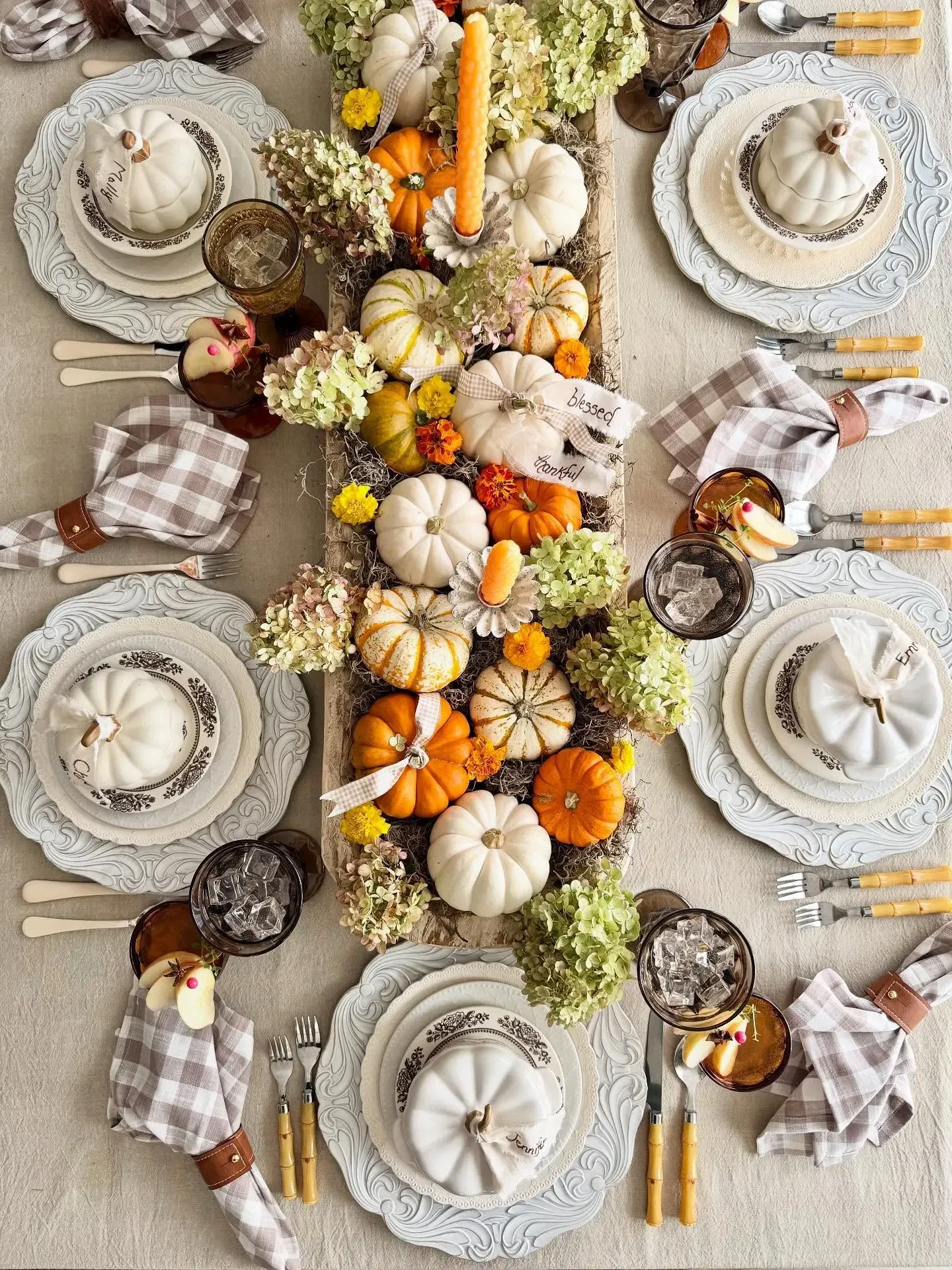 fall table decor ideas with pumpkins, flowers, greenery, taper candles, checked napkins, and layered place settings