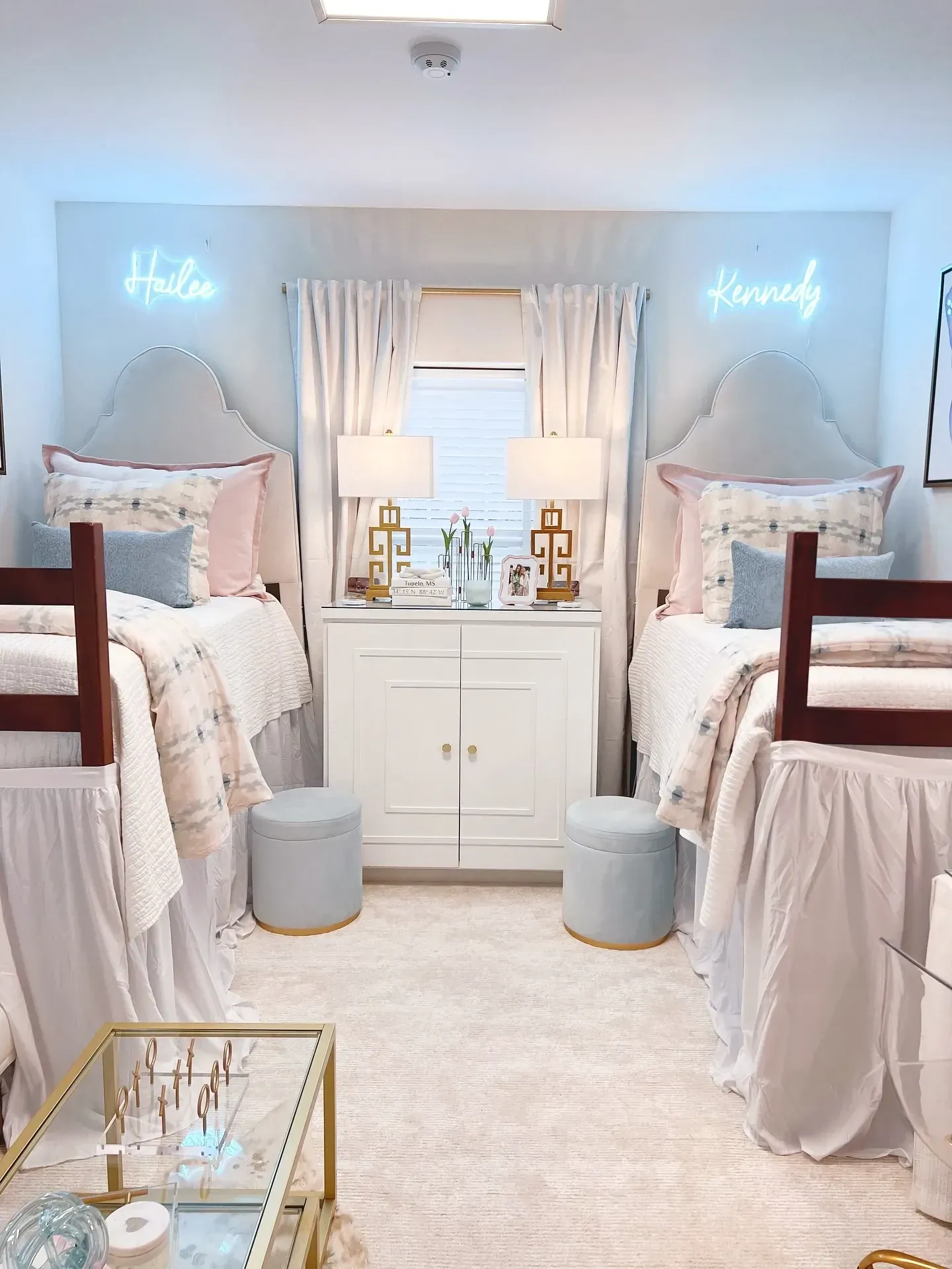pink and blue dorm room ideas with matching neon signs, blue ottomans, pink bedding, white curtains, and gold coffee table