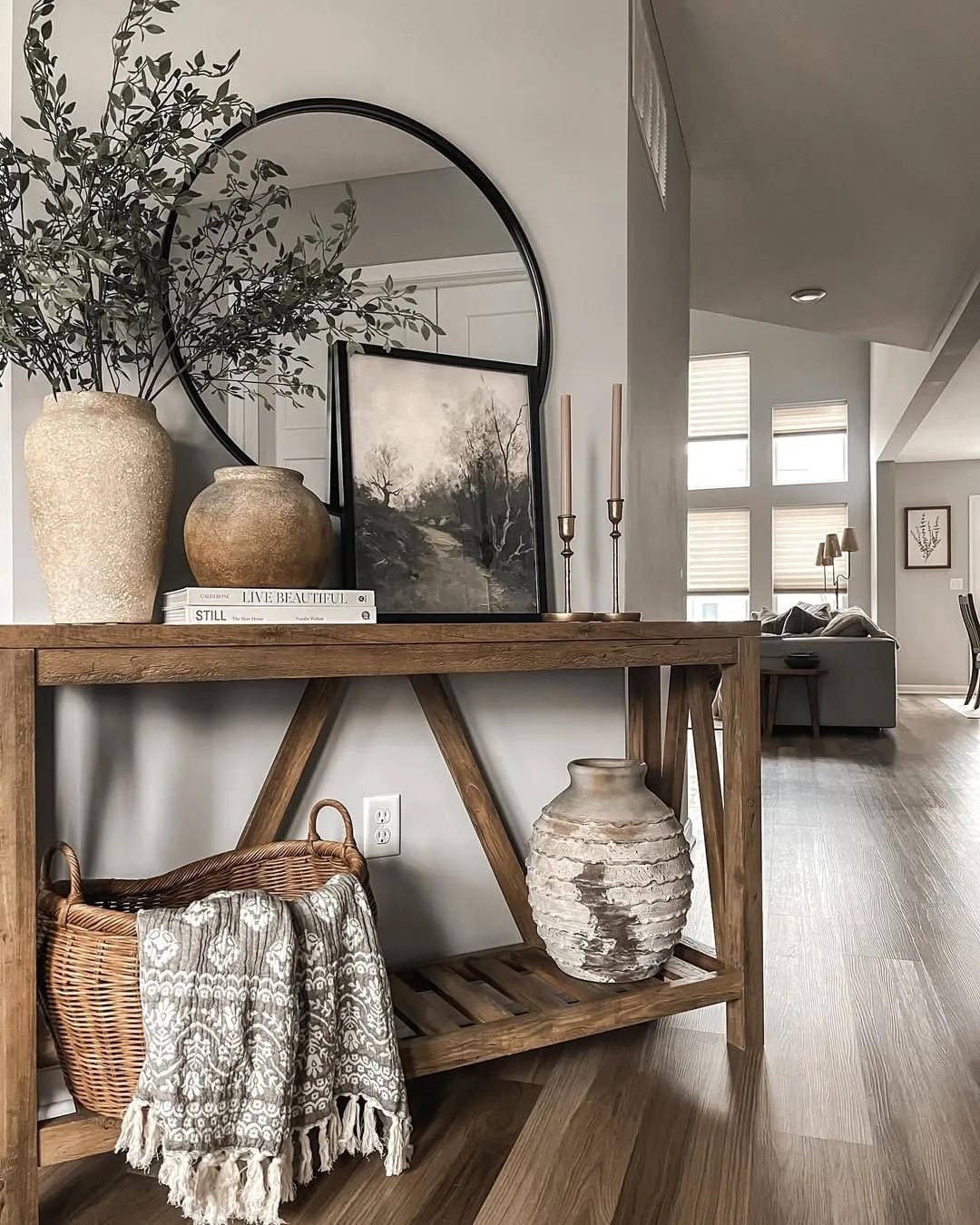 fall entryway table decor ideas with neutral fall styling, arched mirror, dark branches, small pumpkins, baskets, blanket, and wood console