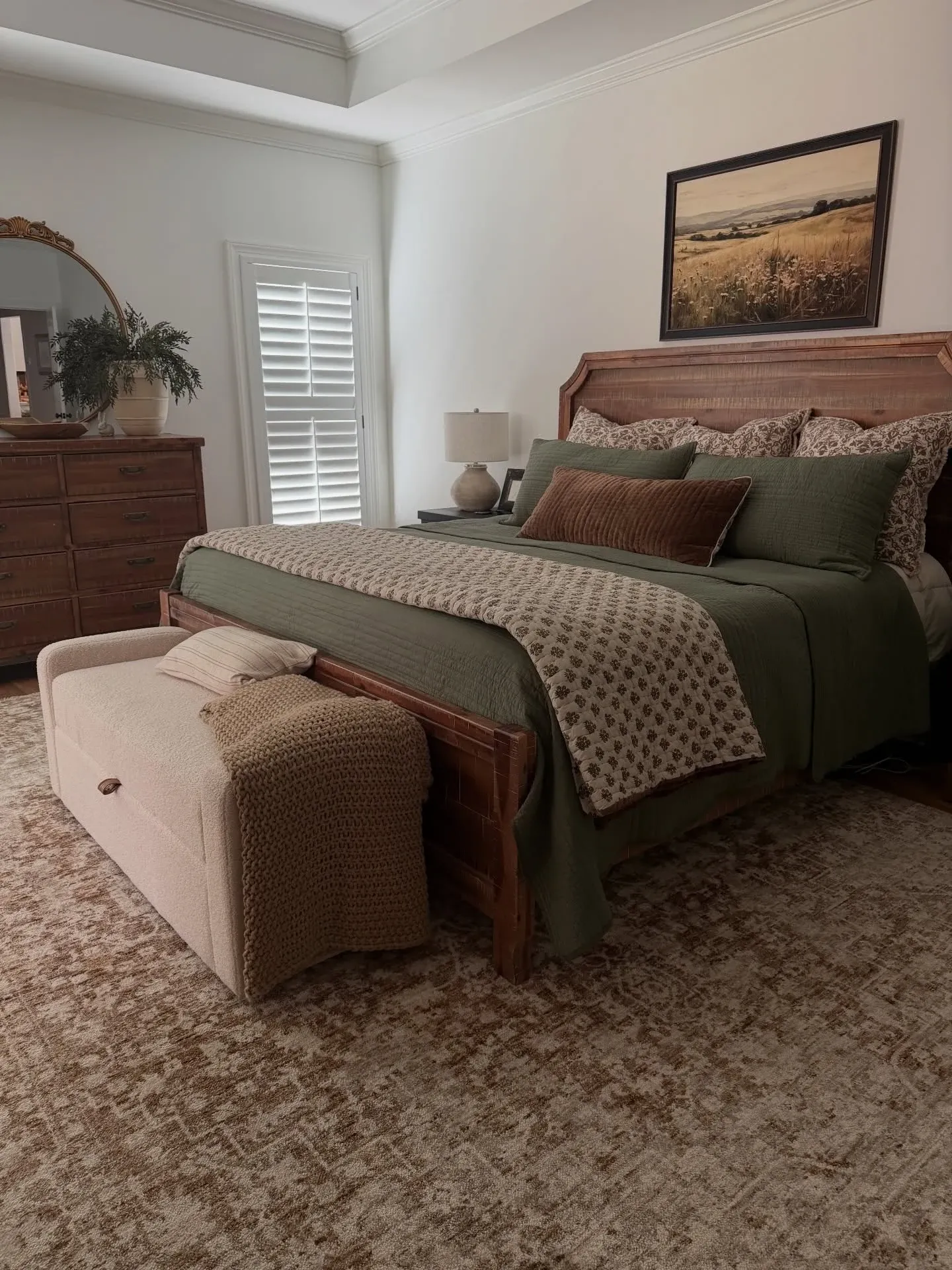 fall bedroom ideas with olive green bedding, brown pillows, plaid blanket, wood dresser, and framed landscape art