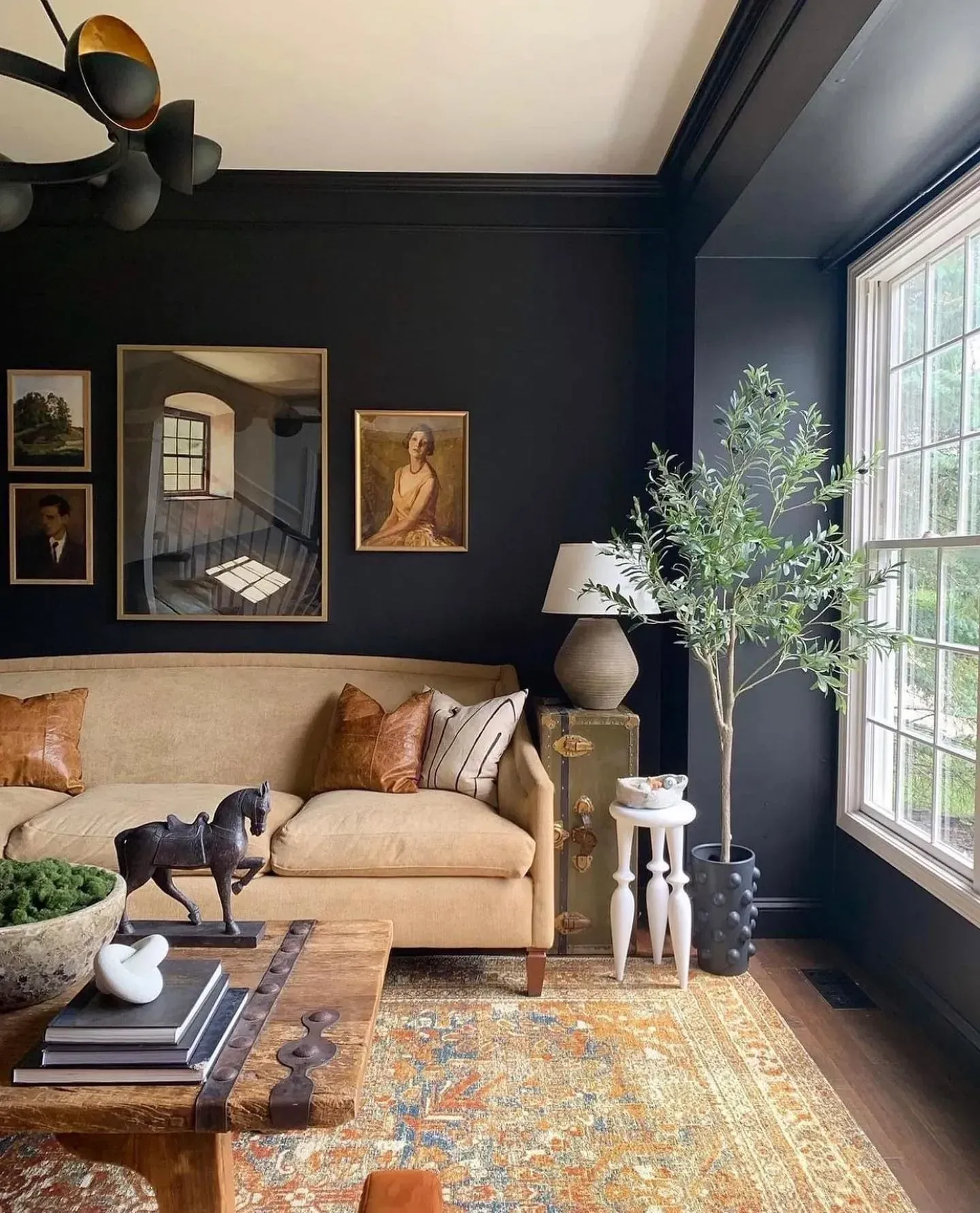 moody living room ideas with near black wall, beige sofa, vintage art, olive tree, and patterned rug