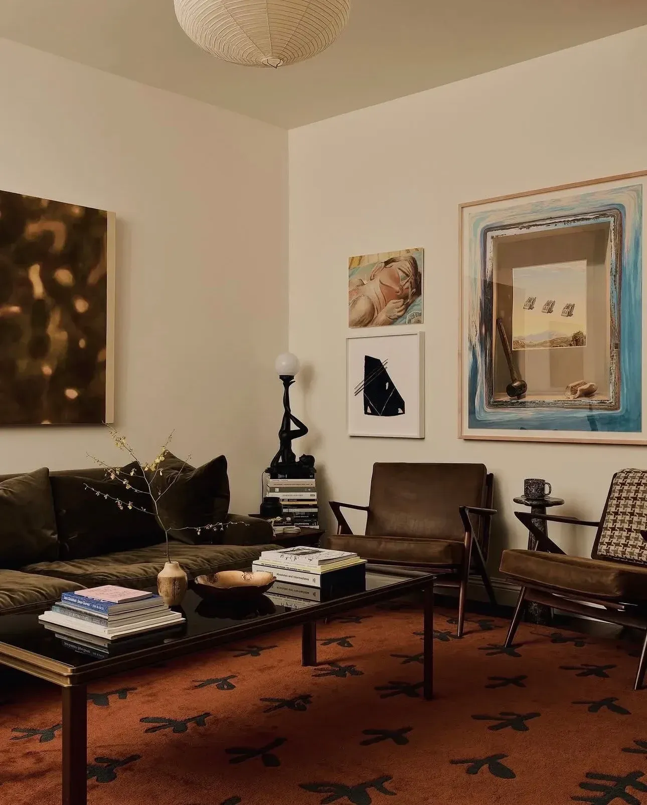 moody living room ideas with patterned rug, black sofa, wood chairs, gallery wall, and coffee table books