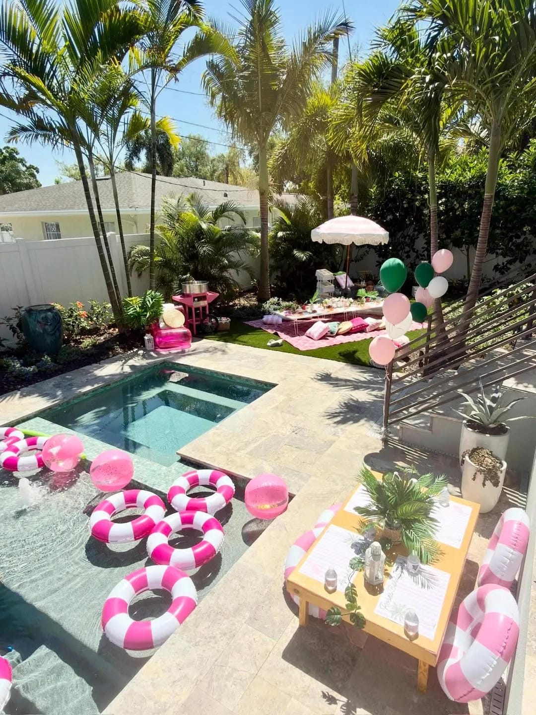 pool party decor ideas with pink and white theme, pool floats, balloons, picnic rug, and tropical backyard setup