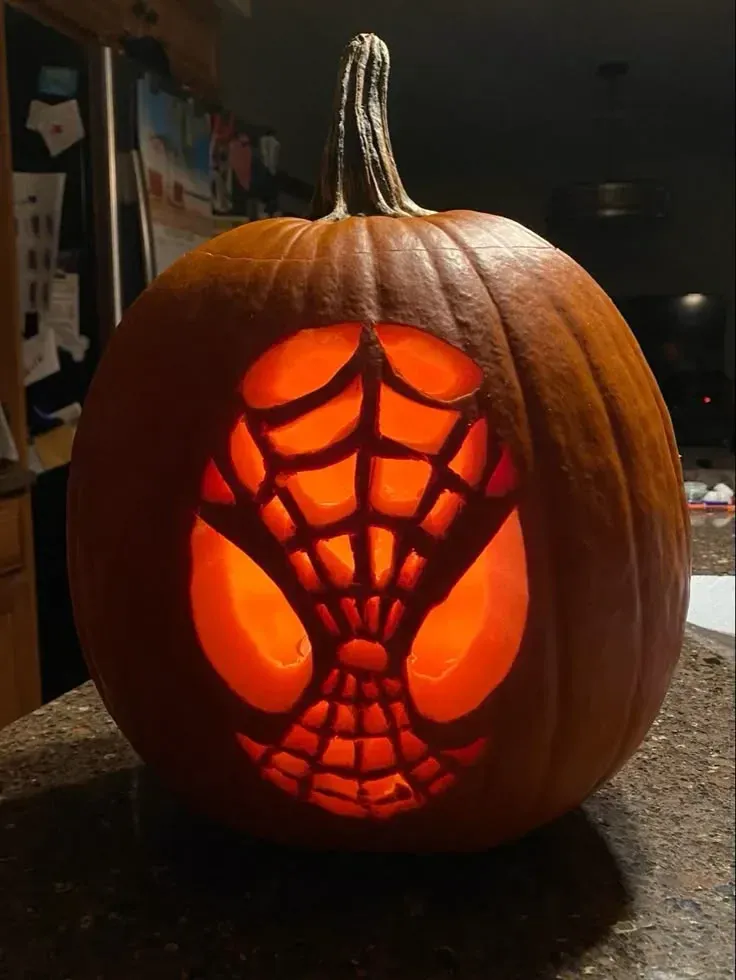 kid friendly pumpkin carving ideas with Spider Man pumpkin, web cutout, glowing eyes, and superhero design